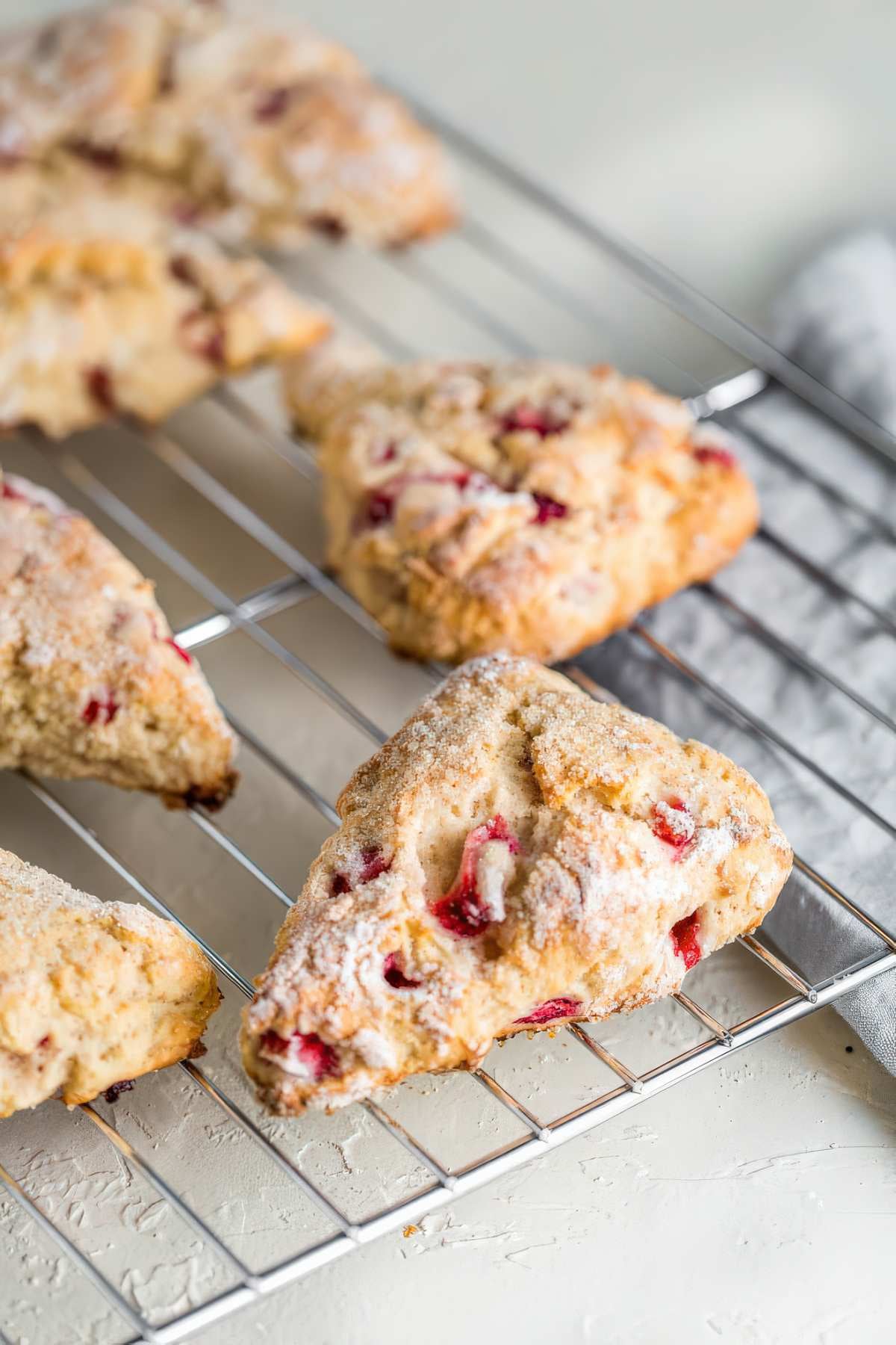 Fresh baked strawberry scones cooling on a rack with visible pieces of strawberries