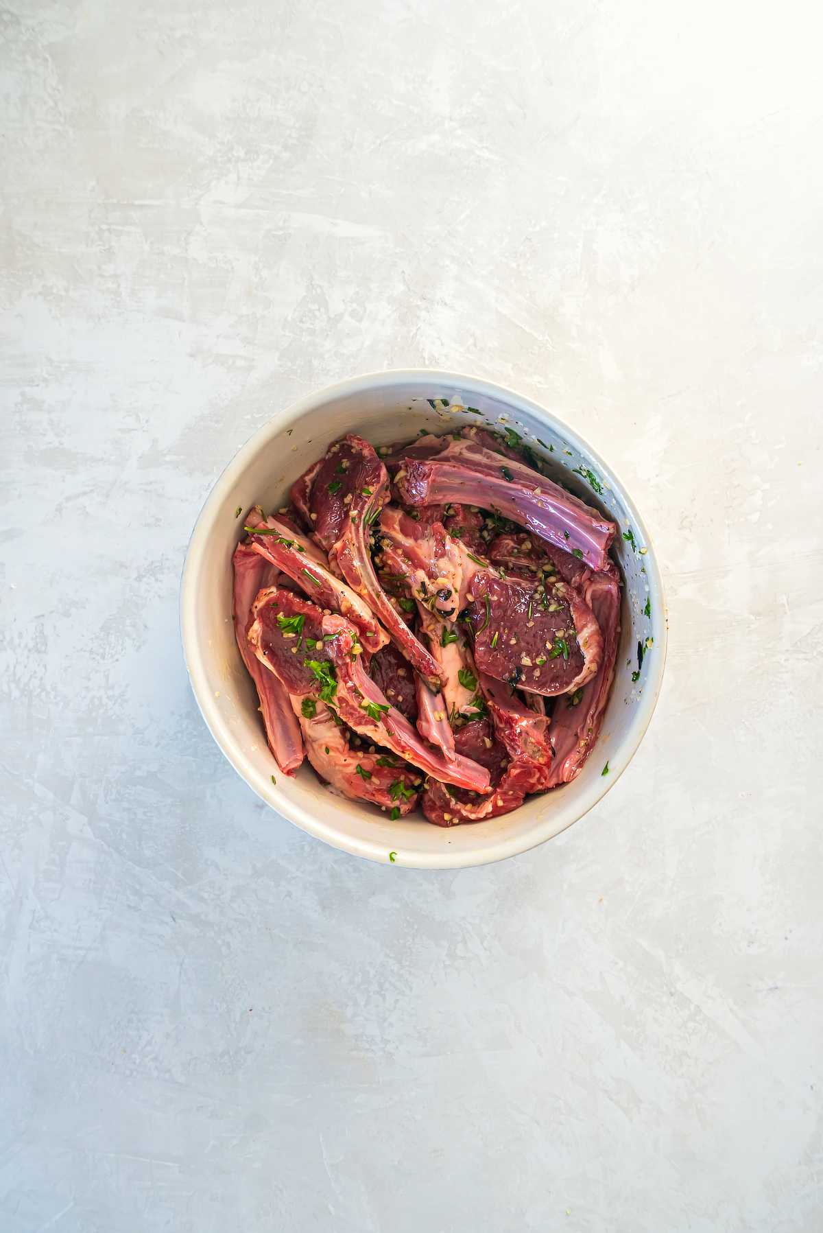 Lamb cutlets coated in garlic herb marinade in a bowl before cooking