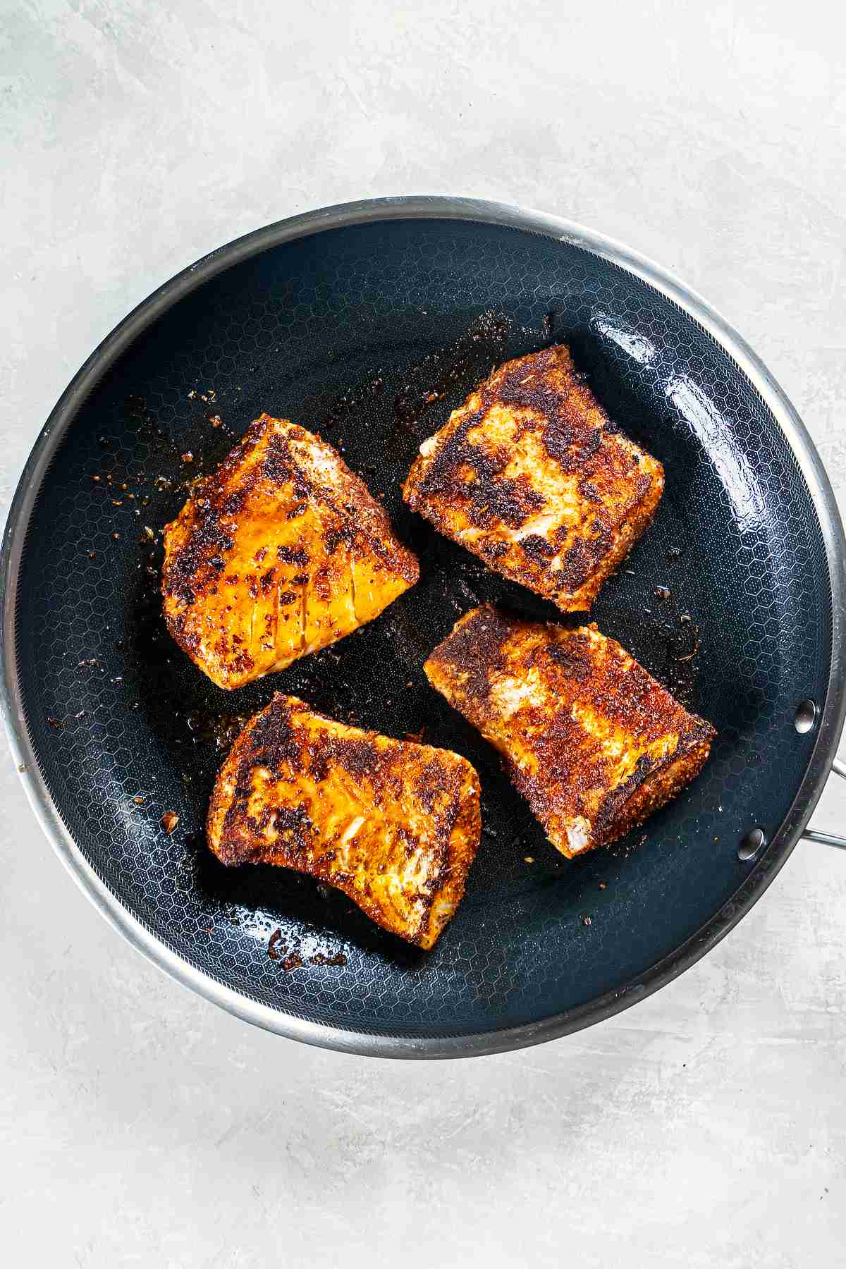 Blackened cod cooking in a skillet with a crispy seasoned crust