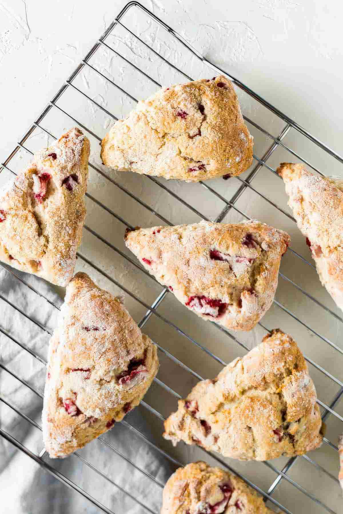Overhead view of strawberry scones cooling on a rack with golden tops and fresh strawberries baked inside