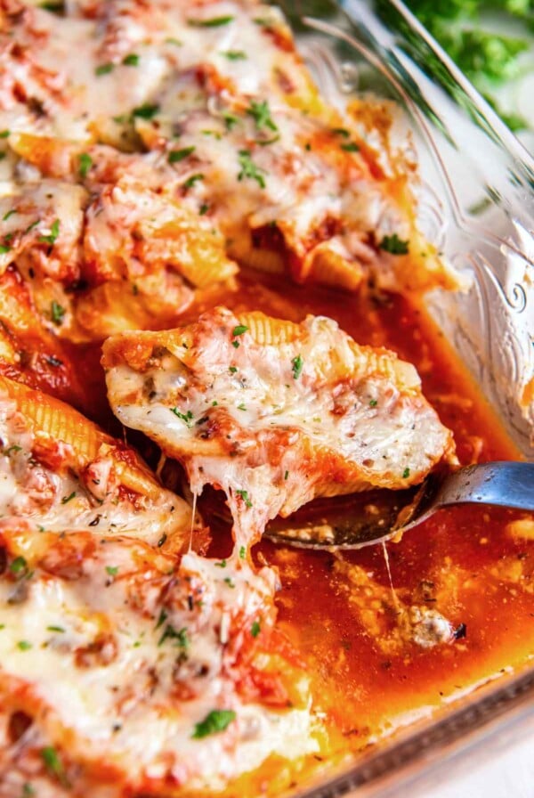 Stuffed shell with ground beef filling lifted from baking dish showing melted cheese and marinara sauce