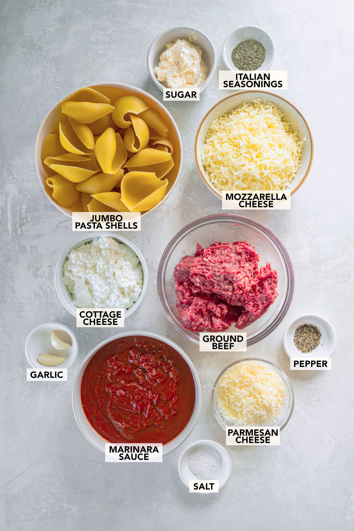 Ingredients for stuffed shells with ground beef including pasta shells, cottage cheese, mozzarella, marinara sauce, and ground beef