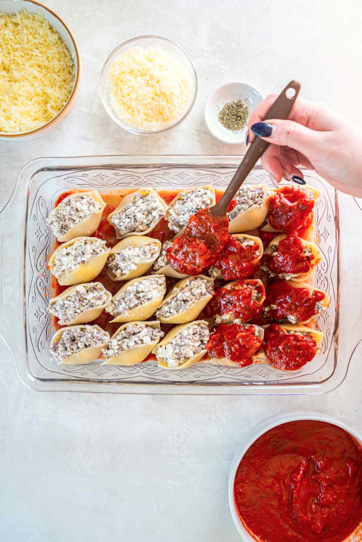 Stuffed shells arranged in baking dish with marinara sauce being added on top