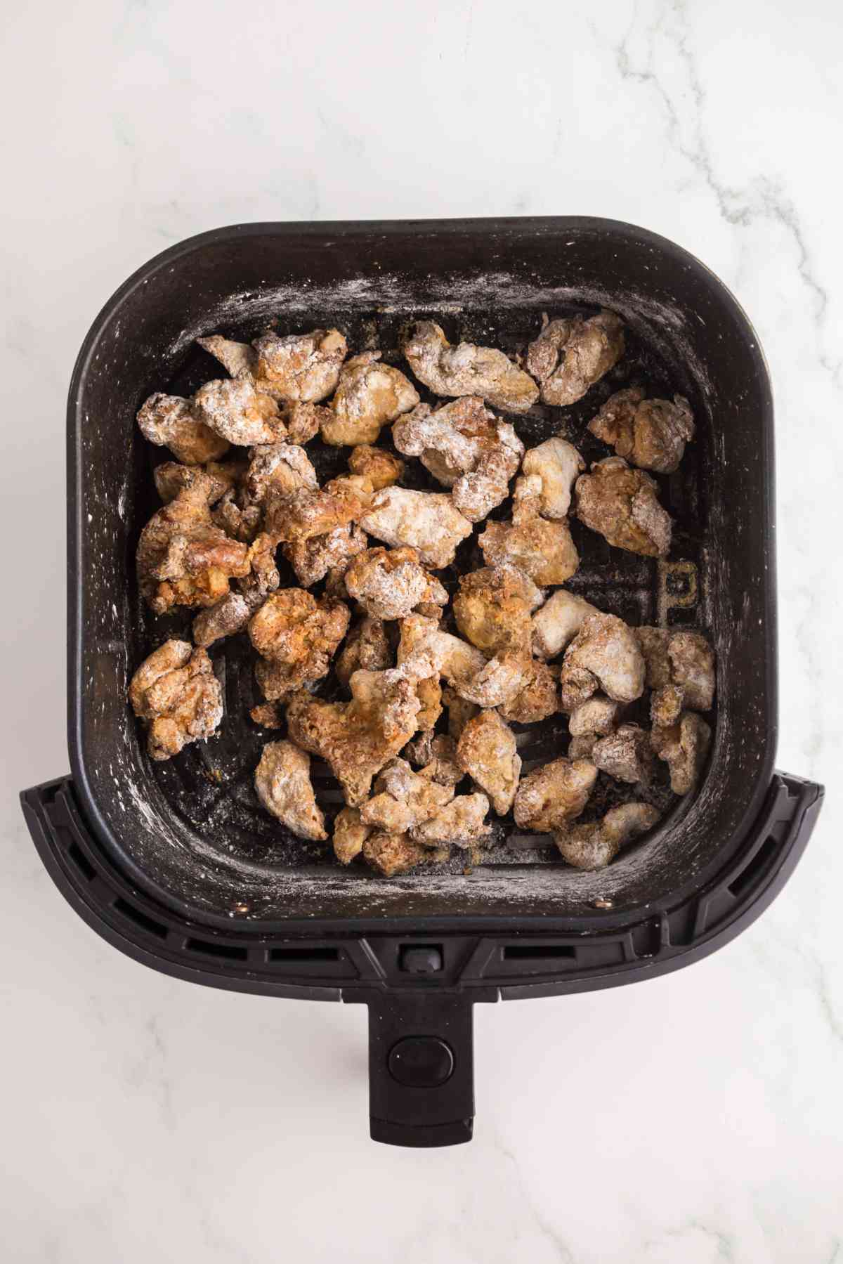 Crispy air fryer chicken pieces cooking in an air fryer basket for Crispy Gochujang Chicken.