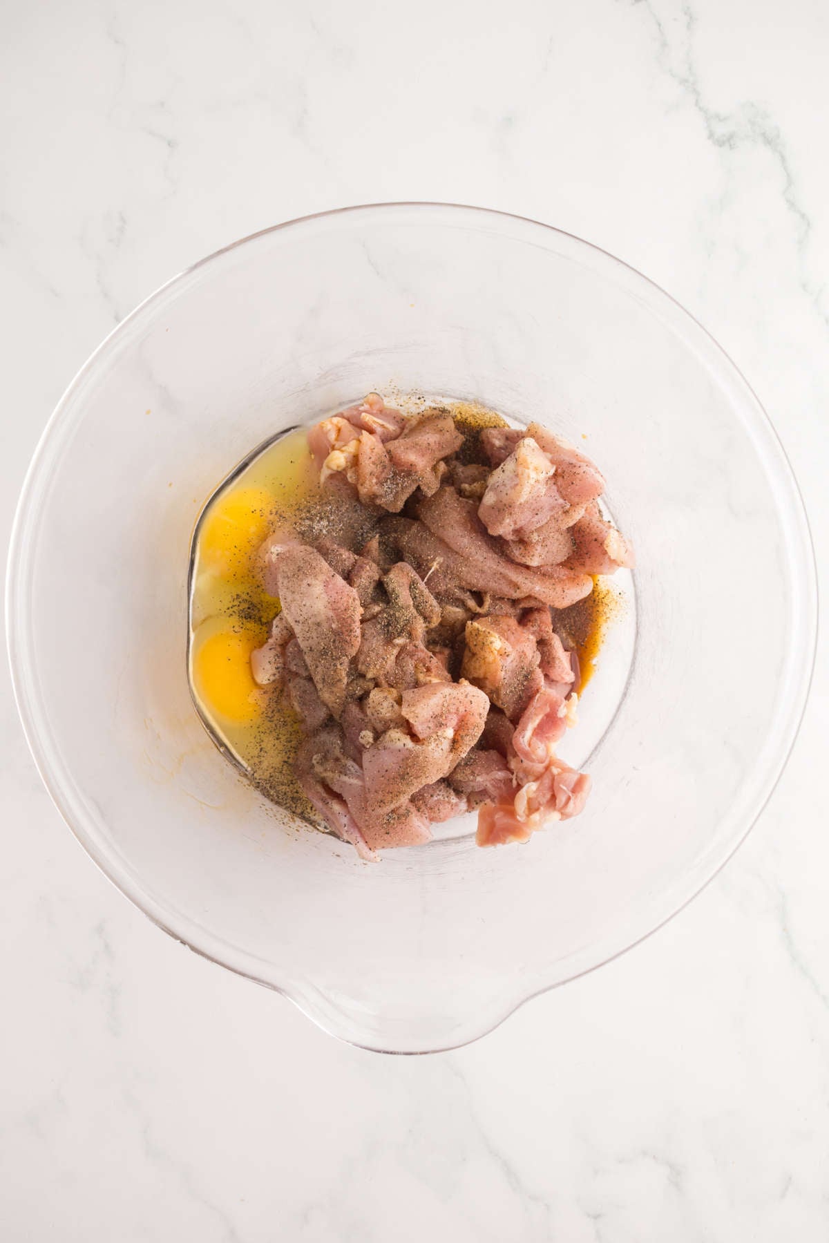 Bite-sized chicken thighs mixed with eggs, soy sauce, and seasonings in a large glass bowl for Crispy Gochujang Chicken.