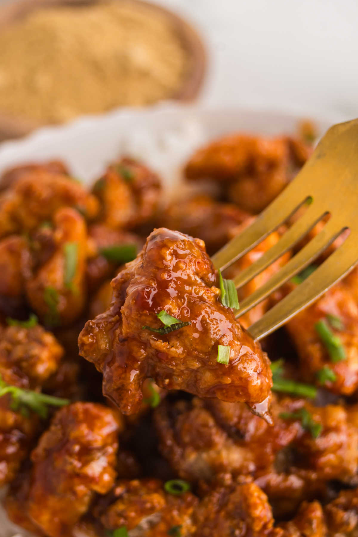 Fork holding a crispy piece of Gochujang Chicken coated in sticky sweet and spicy sauce.