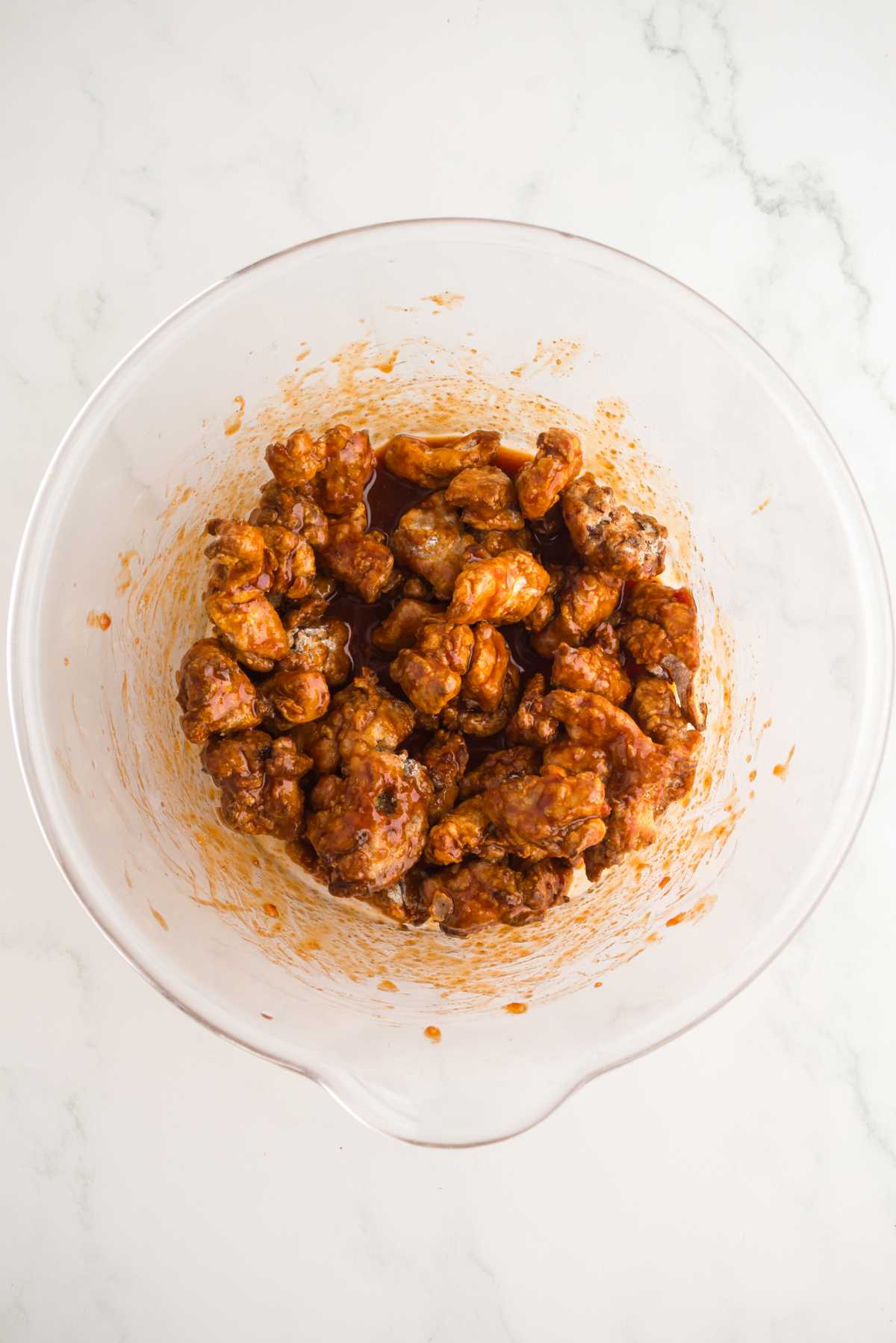 Crispy chicken tossed in sticky gochujang sauce in a large mixing bowl.