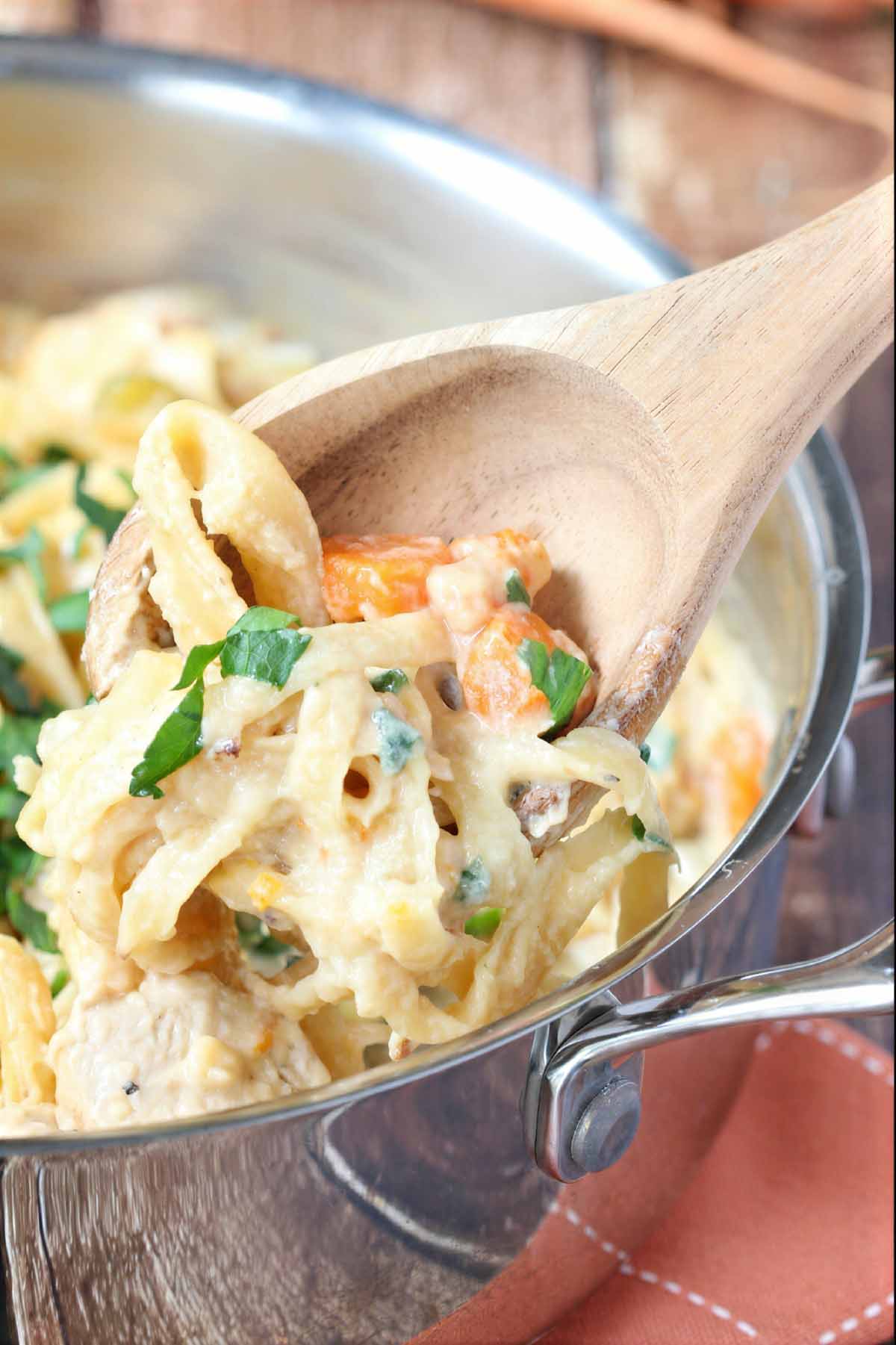 Spoonful of creamy chicken pasta with fettuccine noodles, chicken, carrots, and cheesy sauce.