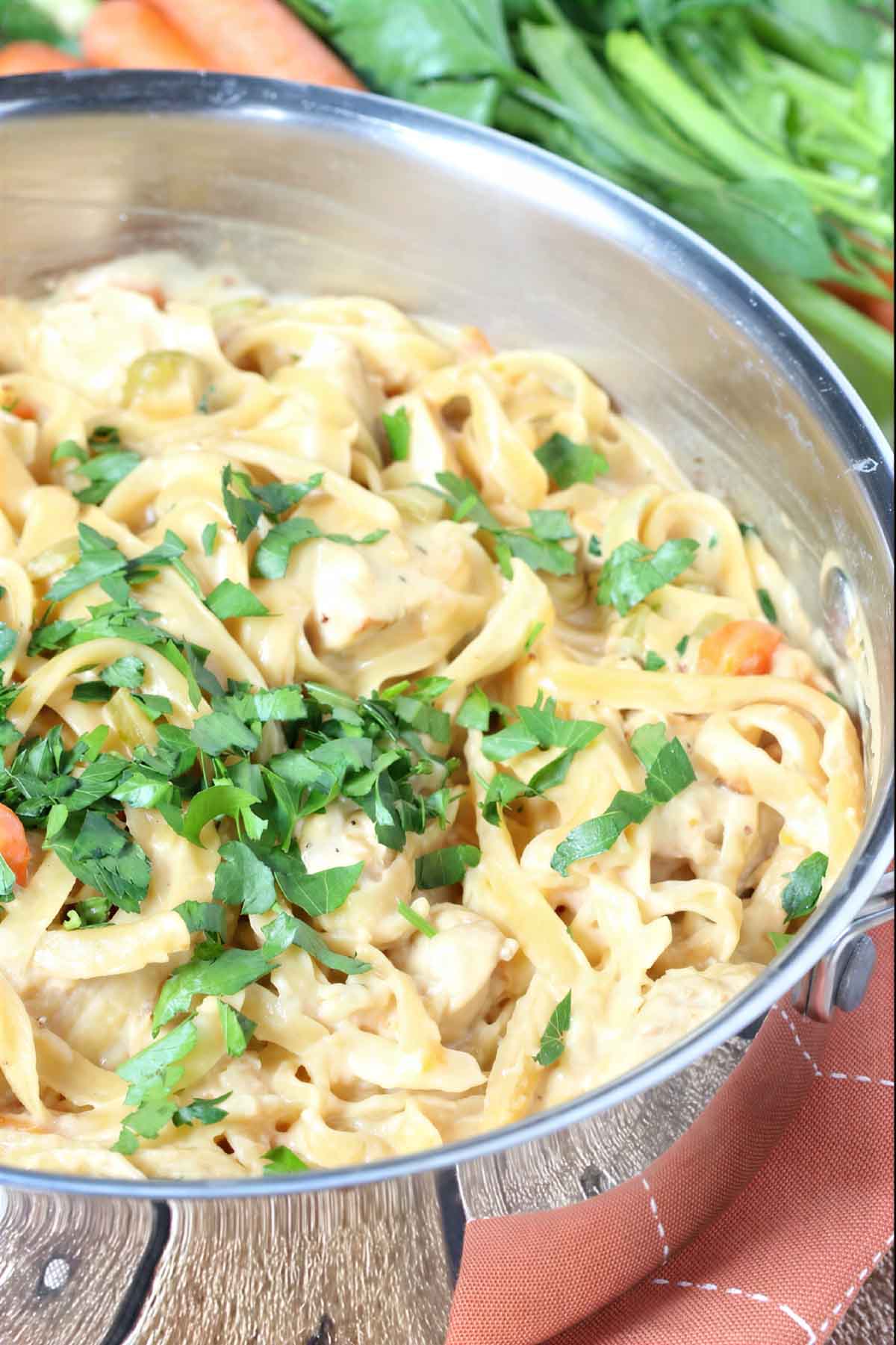 Close-up of creamy one pot chicken pasta with fettuccine noodles, chicken, carrots, and fresh parsley in a skillet.