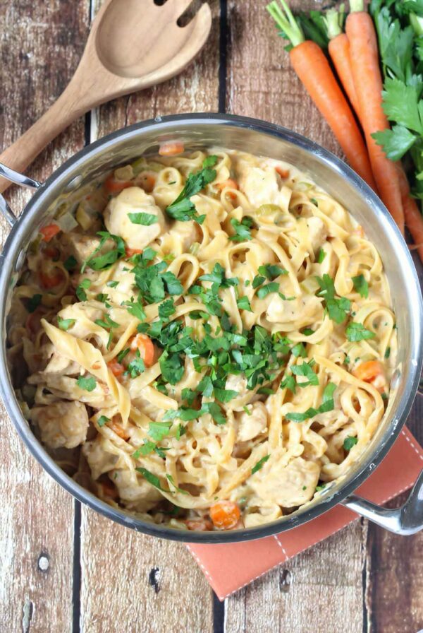 One pot creamy chicken pasta in a skillet topped with fresh parsley and surrounded by carrots and celery.