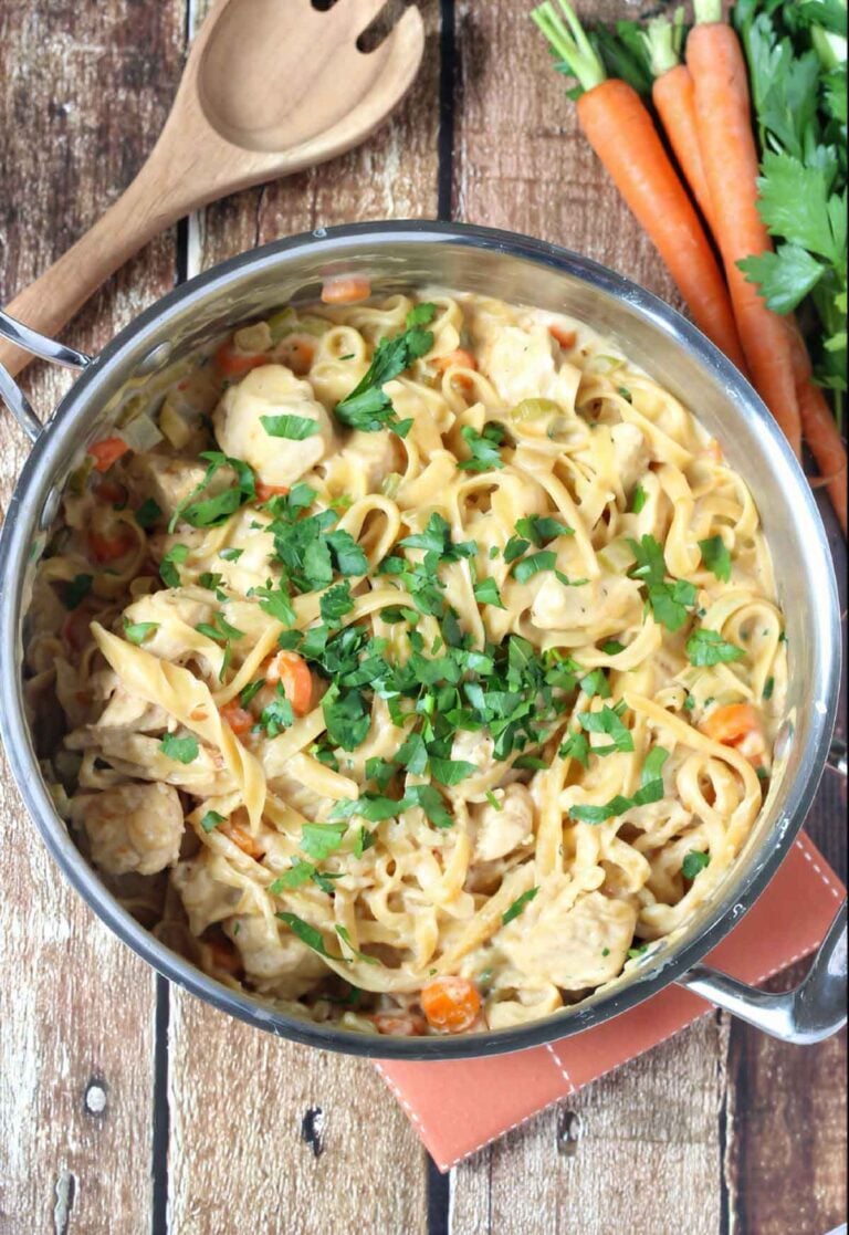 One pot creamy chicken pasta in a skillet topped with fresh parsley and surrounded by carrots and celery.