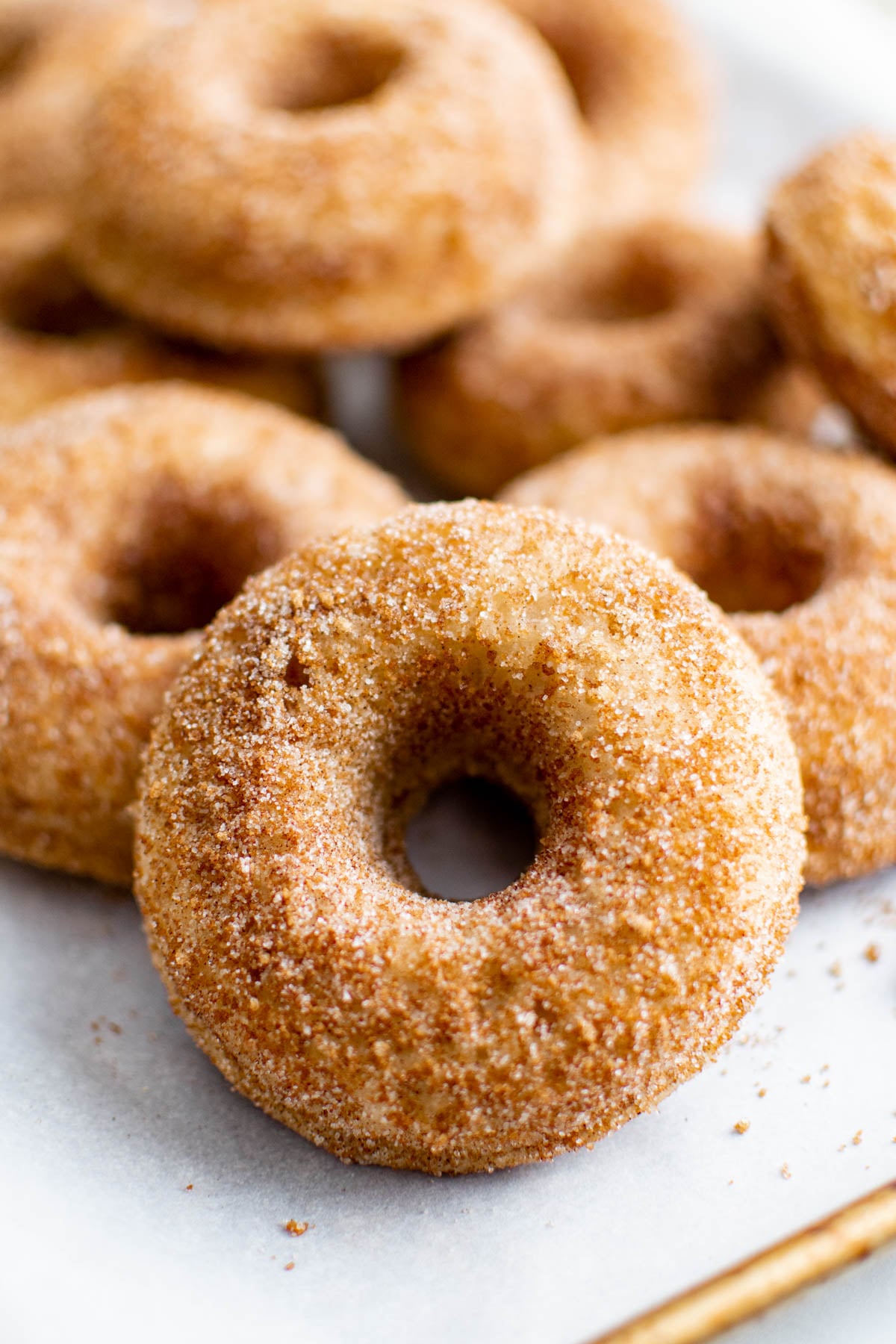 Close-up of a baked apple cider donut coated in cinnamon sugar with additional donuts blurred in the background.