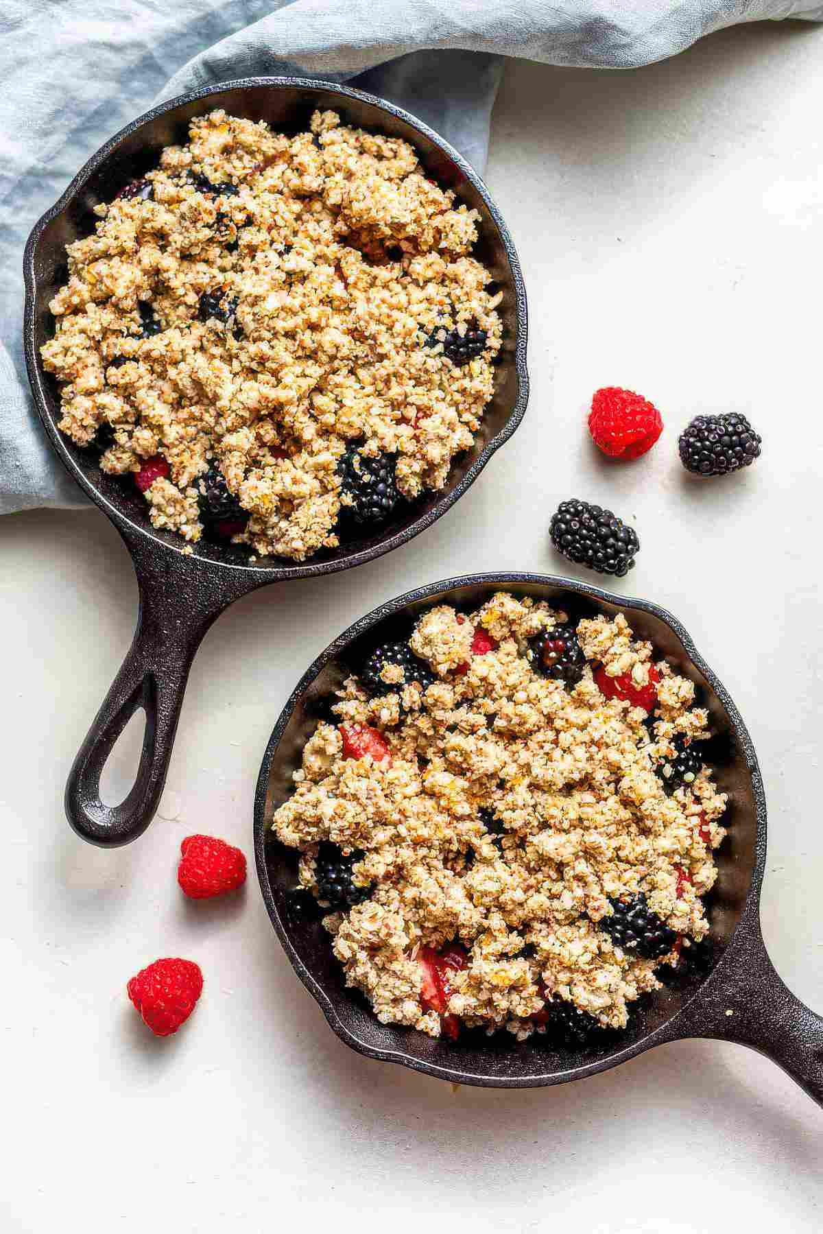 Two cast iron skillets filled with fresh berries and almond oat topping before baking.