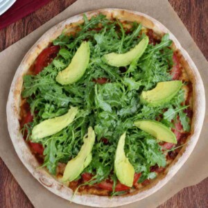 Overhead view of California BLT pizza topped with chicken, bacon, mozzarella cheese, tomatoes, avocado and arugula.
