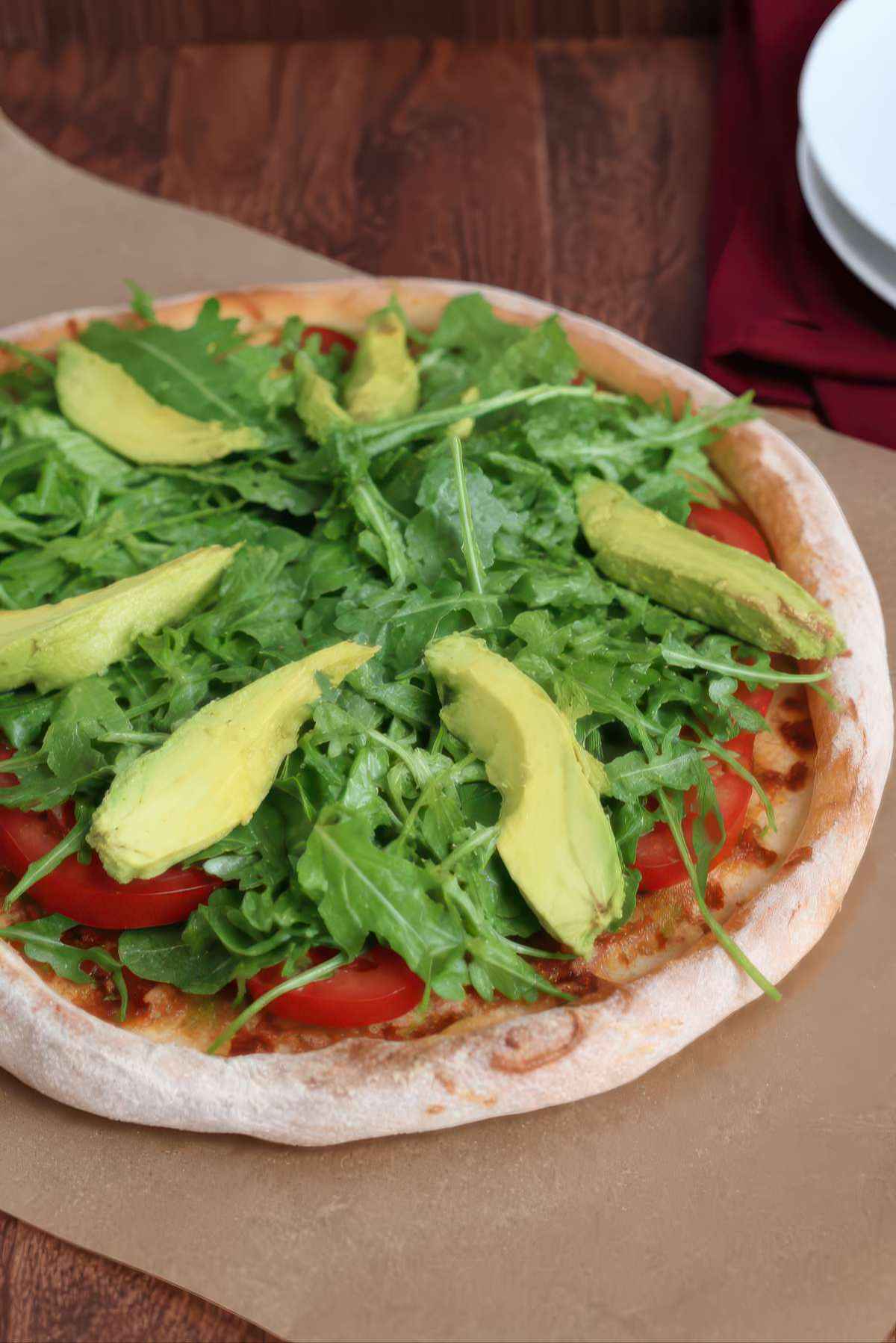Close-up view of California BLT pizza topped with fresh arugula, avocado slices and tomatoes on a thin pizza crust.