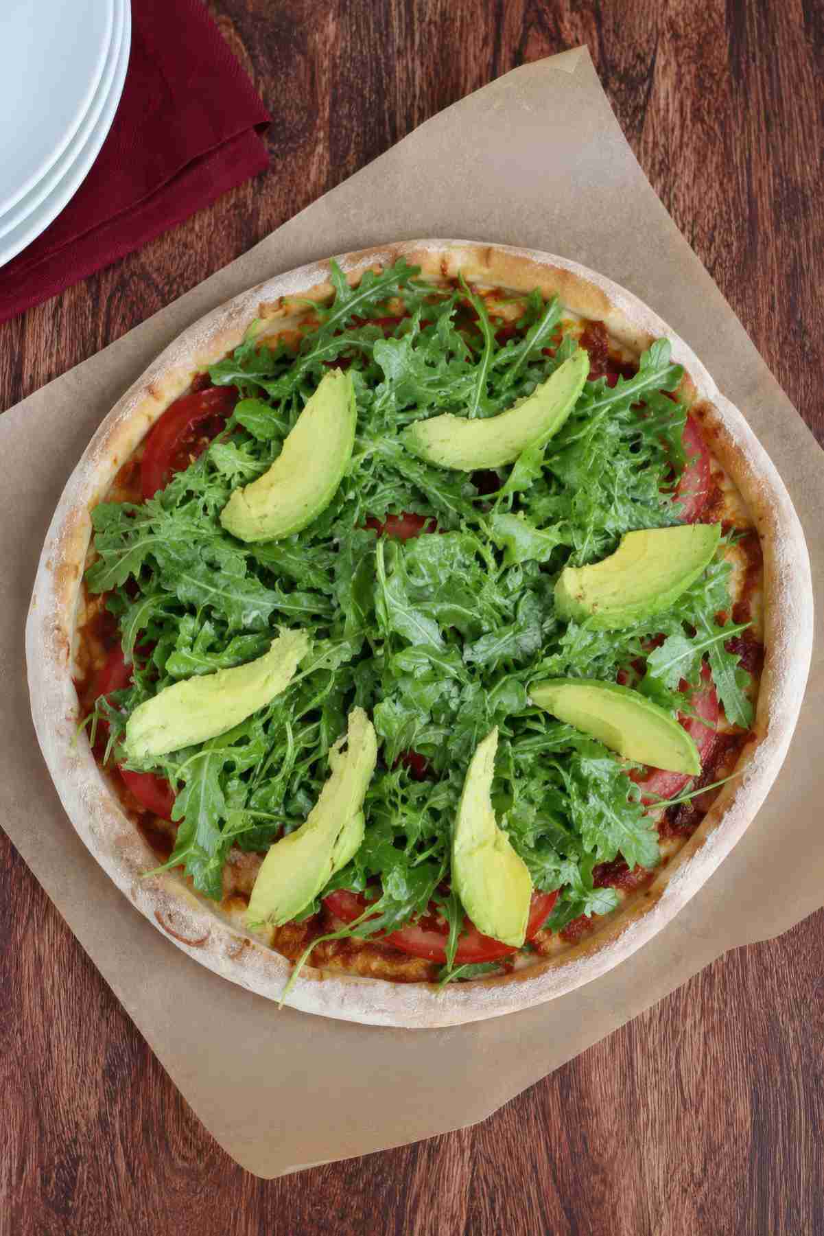 Overhead view of California BLT pizza topped with chicken, bacon, mozzarella cheese, tomatoes, avocado and arugula.