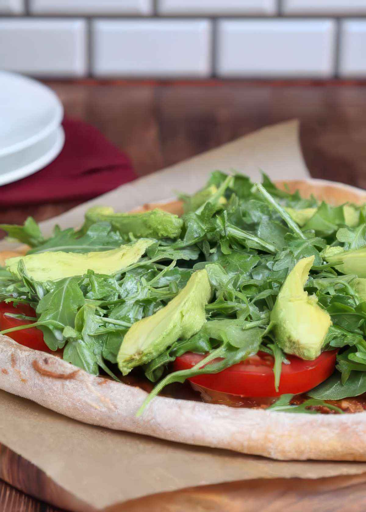 Side view of California BLT pizza with avocado, tomatoes and arugula layered over melted cheese and bacon.