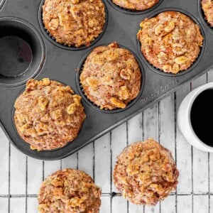 Freshly baked pumpkin muffins topped with golden brown pecan streusel cooling in a muffin pan.