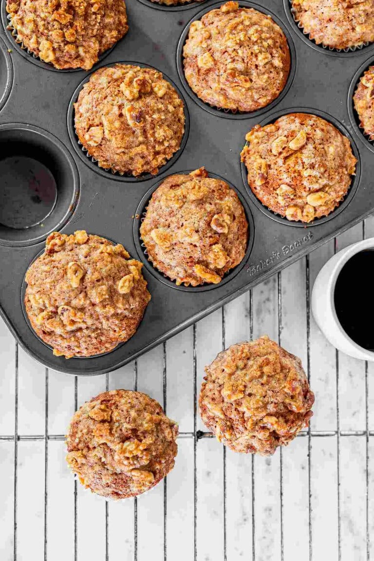 Freshly baked pumpkin muffins topped with golden brown pecan streusel cooling in a muffin pan.