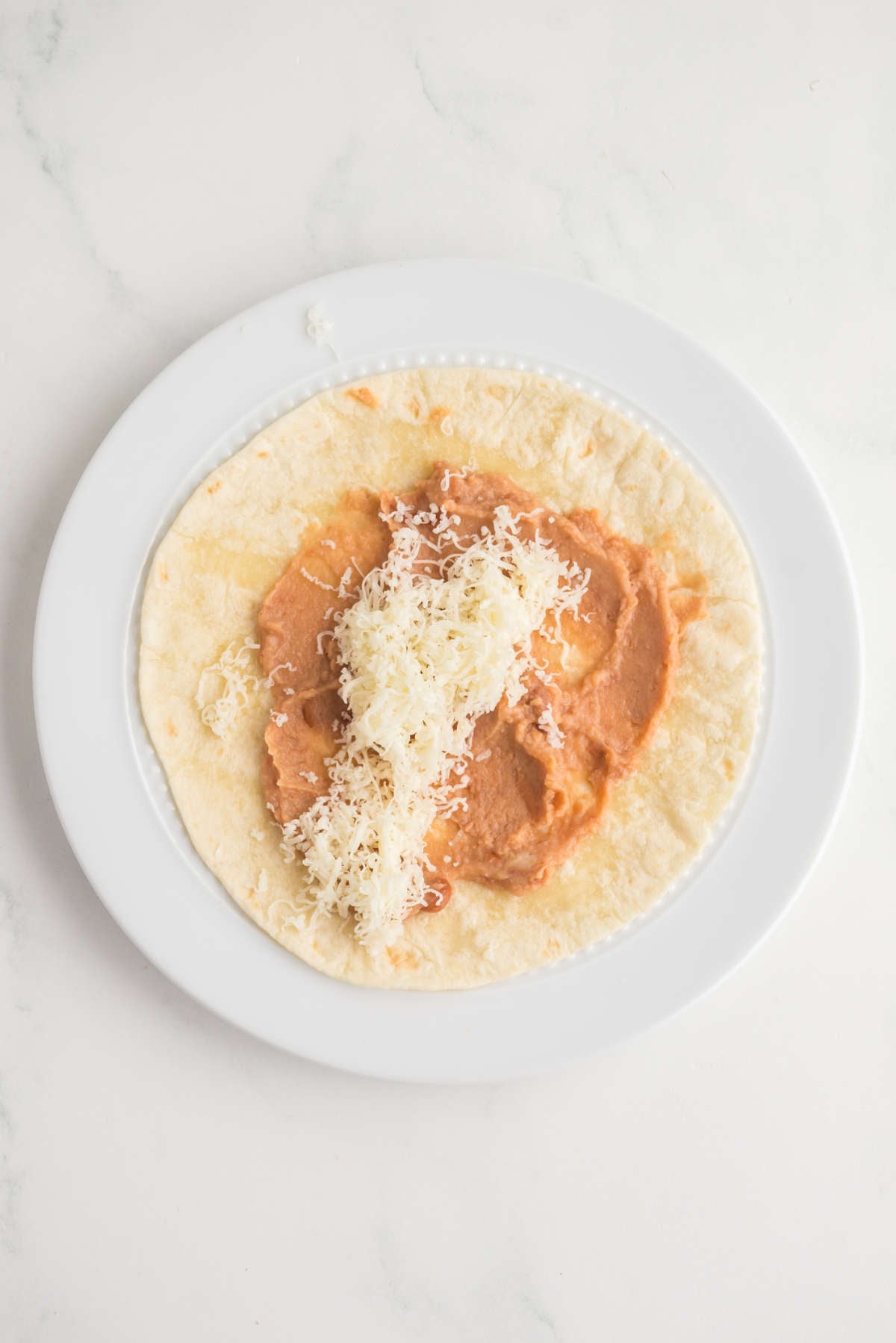 Refried beans and shredded cheese spread on a tortilla to make bean and cheese taquitos
