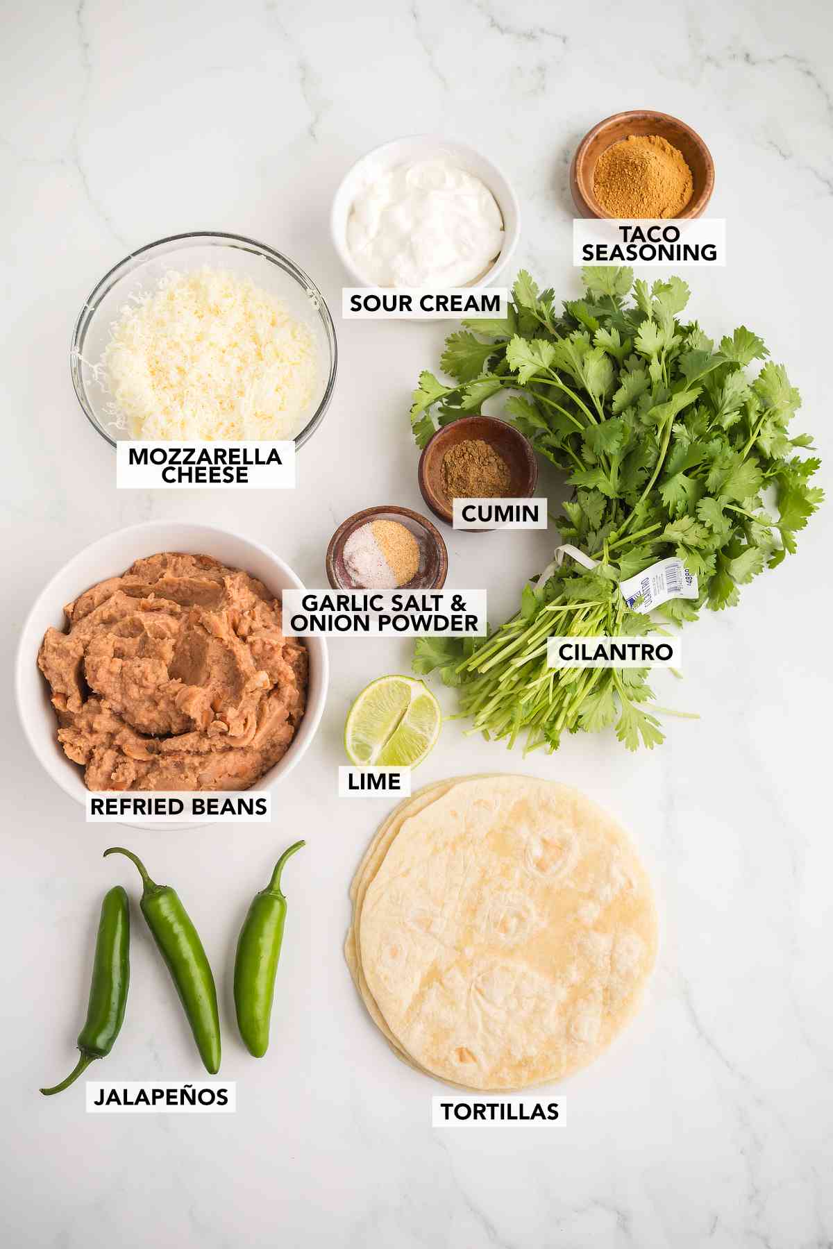 Ingredients for bean and cheese taquitos including refried beans, mozzarella cheese, tortillas, jalapeños, cilantro, sour cream, and spices