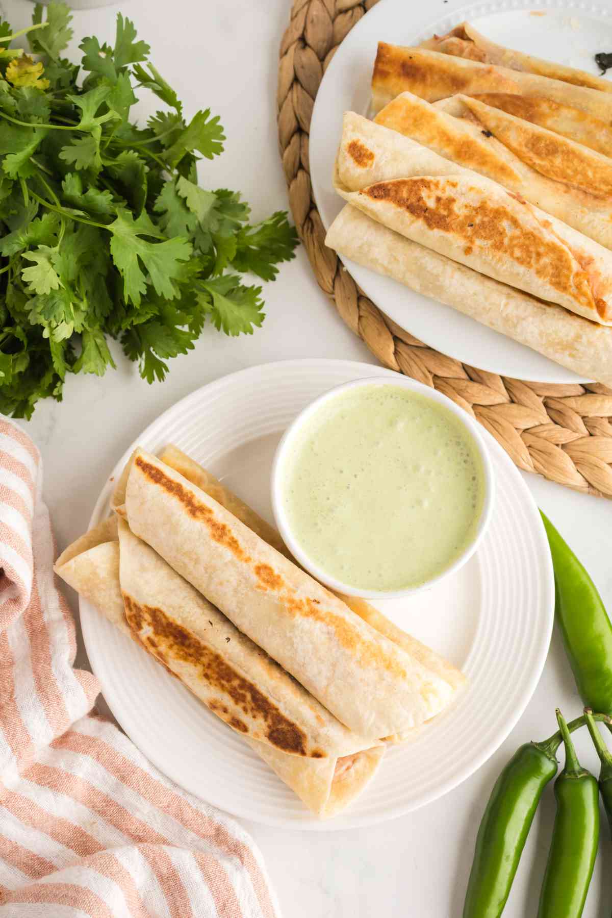 Bean and cheese taquitos on a plate with creamy jalapeño ranch sauce and fresh cilantro