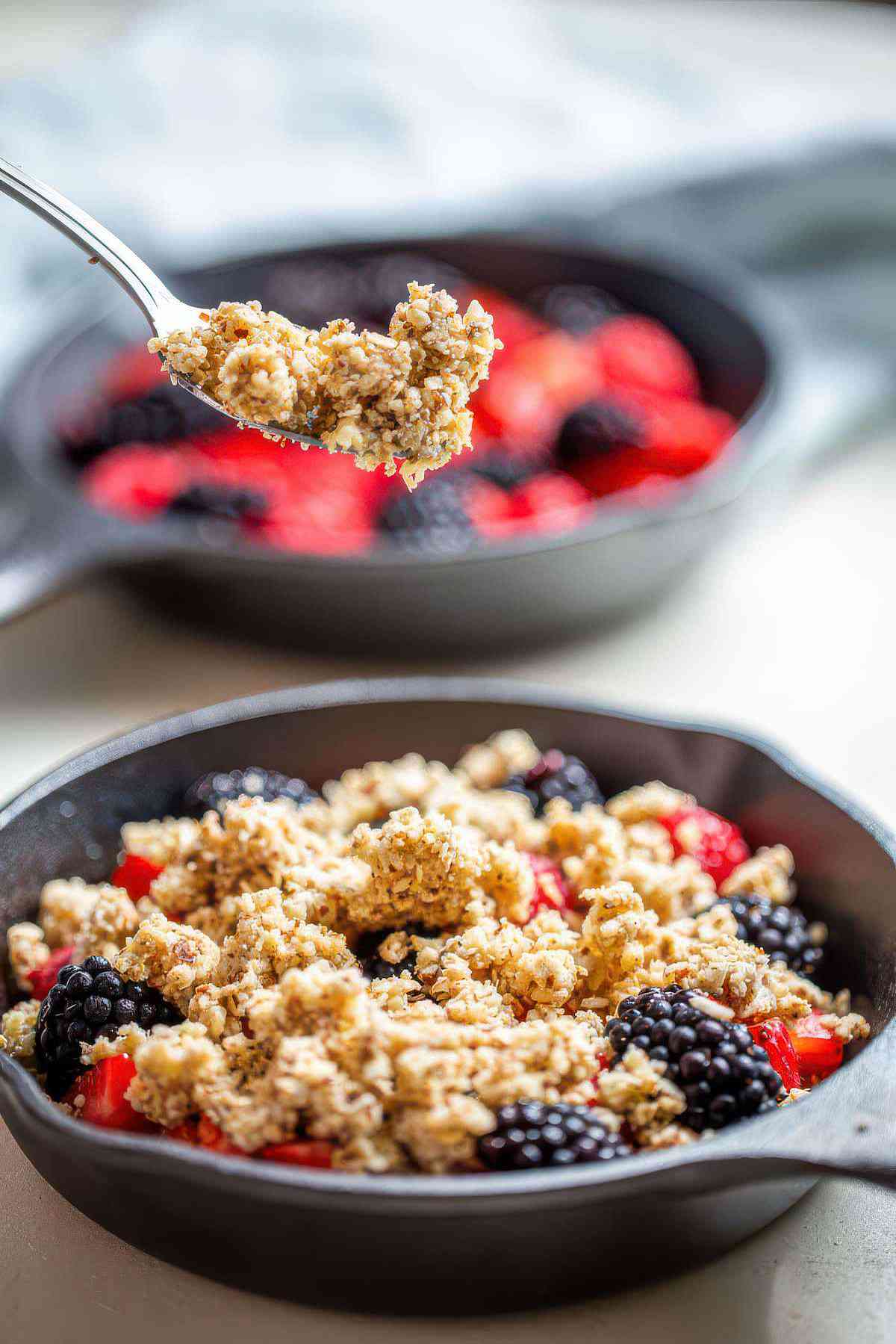 Fresh berries topped with almond oat crumble in a mini cast iron skillet before baking.