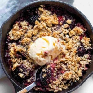 Berry almond crisp baked in a cast iron skillet and topped with a scoop of vanilla ice cream.