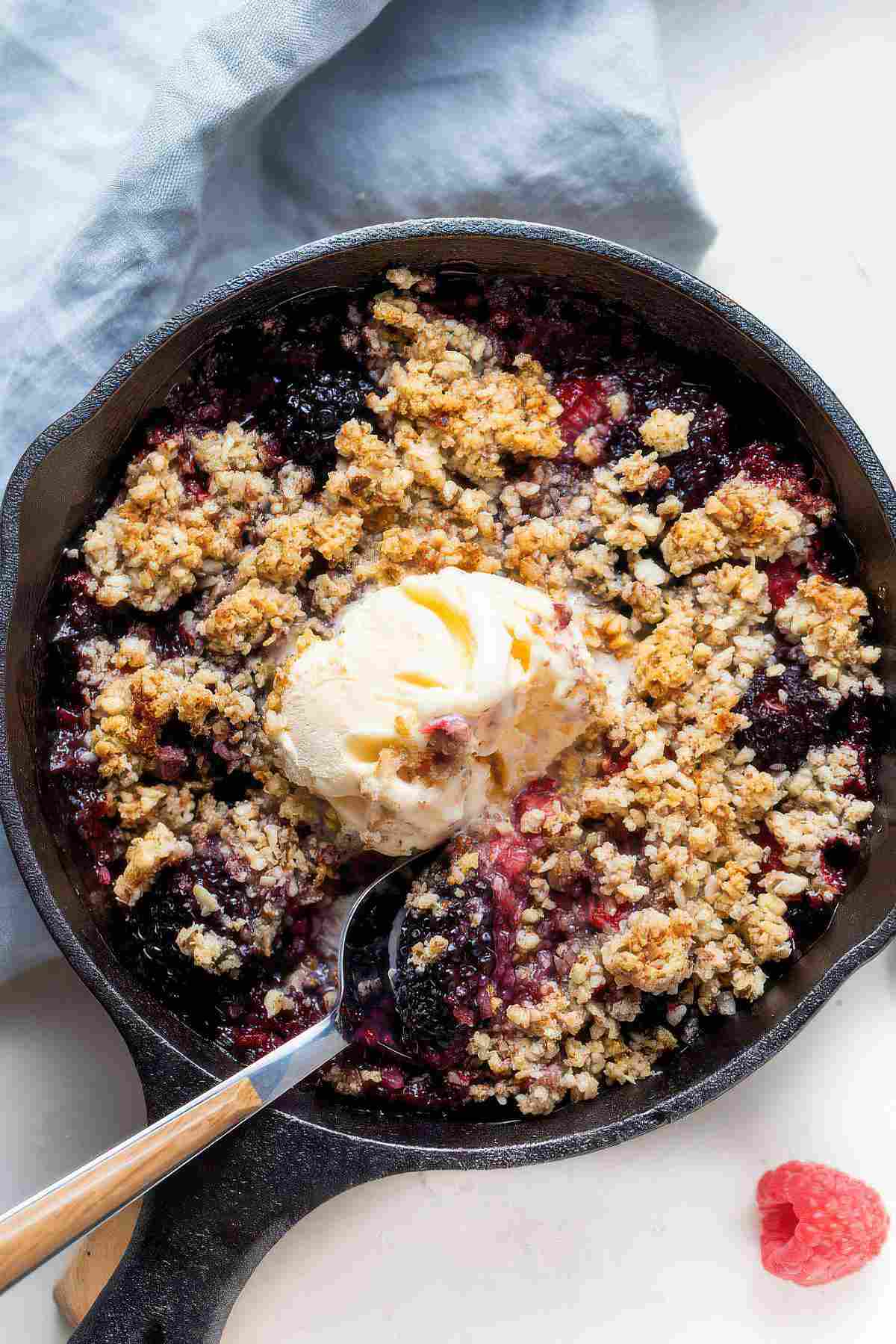 Berry almond crisp baked in a cast iron skillet and topped with a scoop of vanilla ice cream.