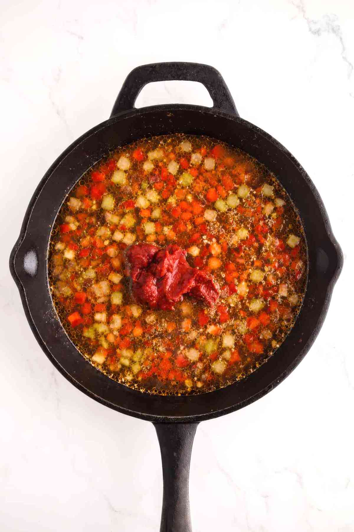 Chicken broth and tomato paste added to sautéed vegetables in a skillet for Cajun chicken orzo.