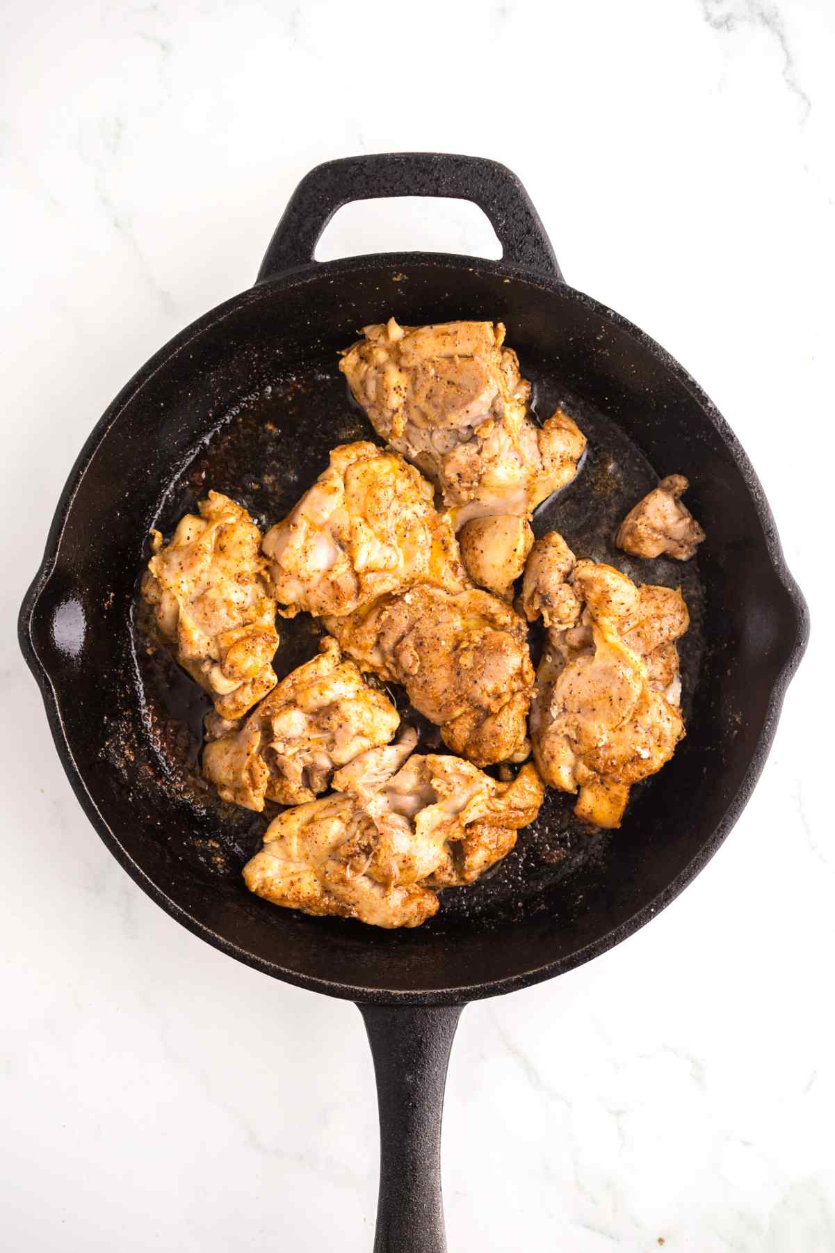Seasoned chicken thighs cooking in a cast iron skillet for creamy Cajun chicken orzo.
