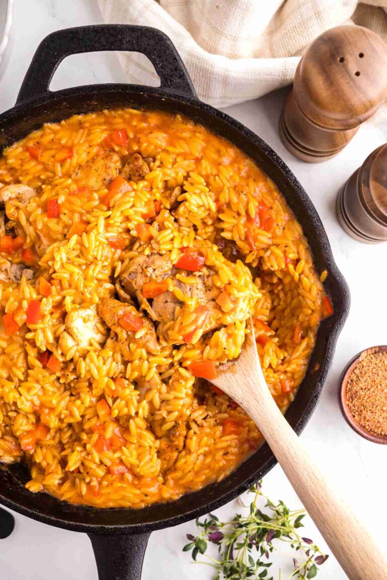 Creamy Cajun chicken orzo in a cast iron skillet with tender chicken, orzo pasta, Cajun seasoning, and red bell peppers.