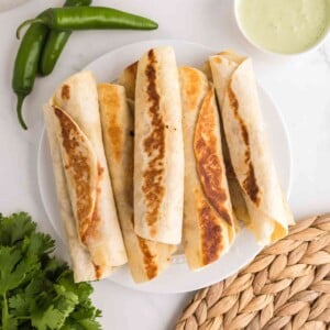 Crispy bean and cheese taquitos served on a plate with jalapeño ranch dipping sauce and fresh jalapeños