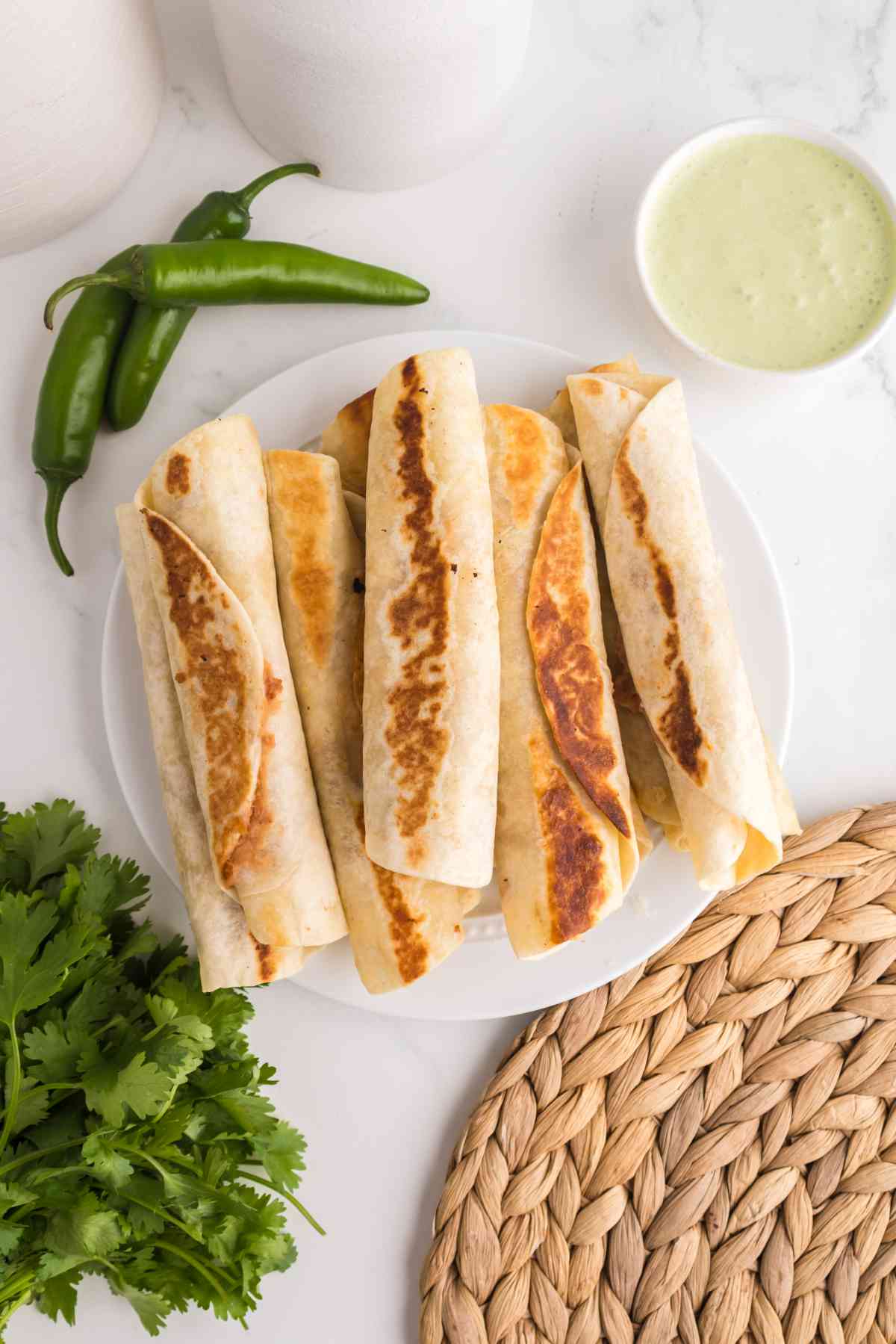 Crispy bean and cheese taquitos served on a plate with jalapeño ranch dipping sauce and fresh jalapeños