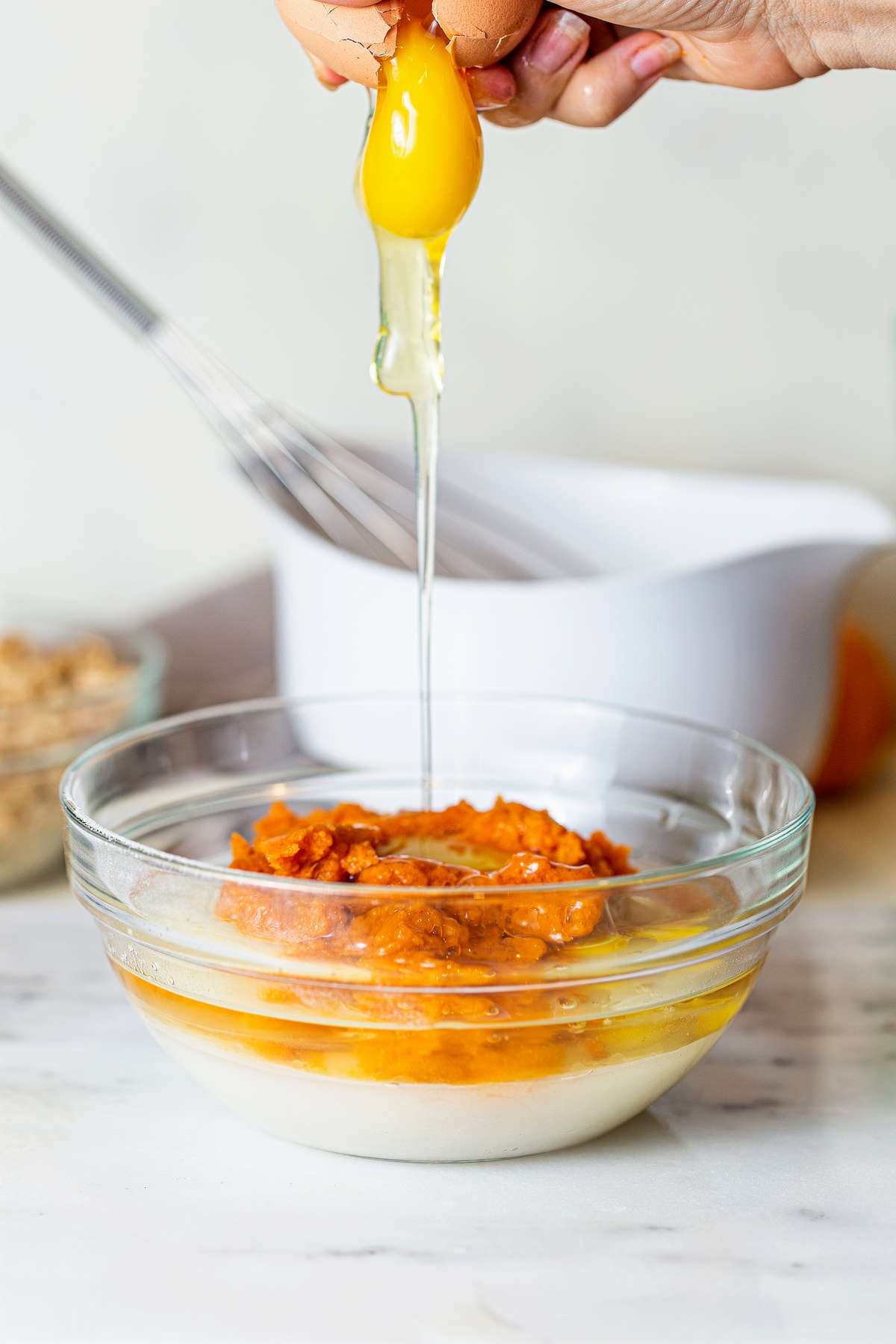 dding an egg to pumpkin puree and wet ingredients while making pumpkin muffin batter.