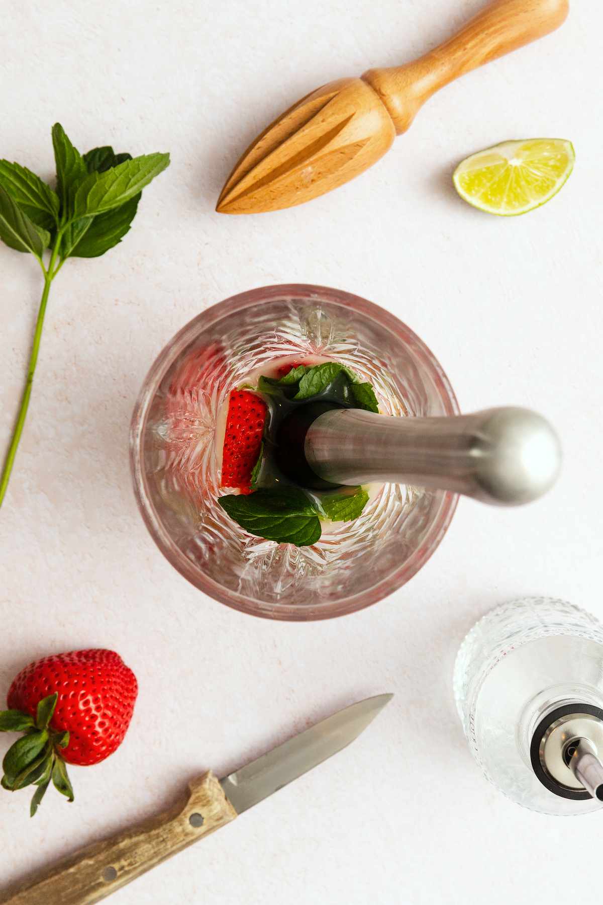 Muddling fresh strawberries and mint leaves in a mixing glass to make a strawberry mojito.