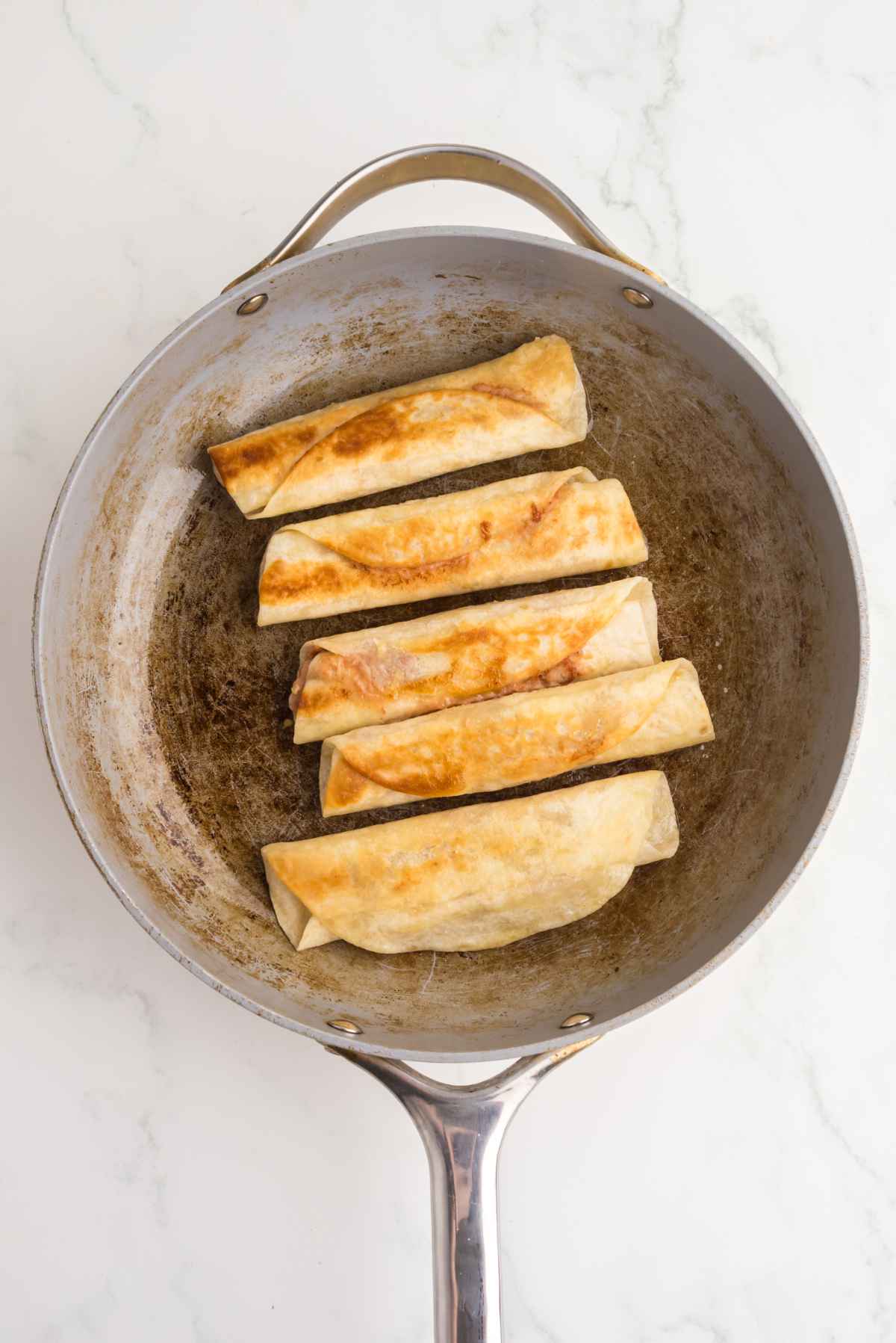 Bean and cheese taquitos cooking in a skillet until golden and crispy