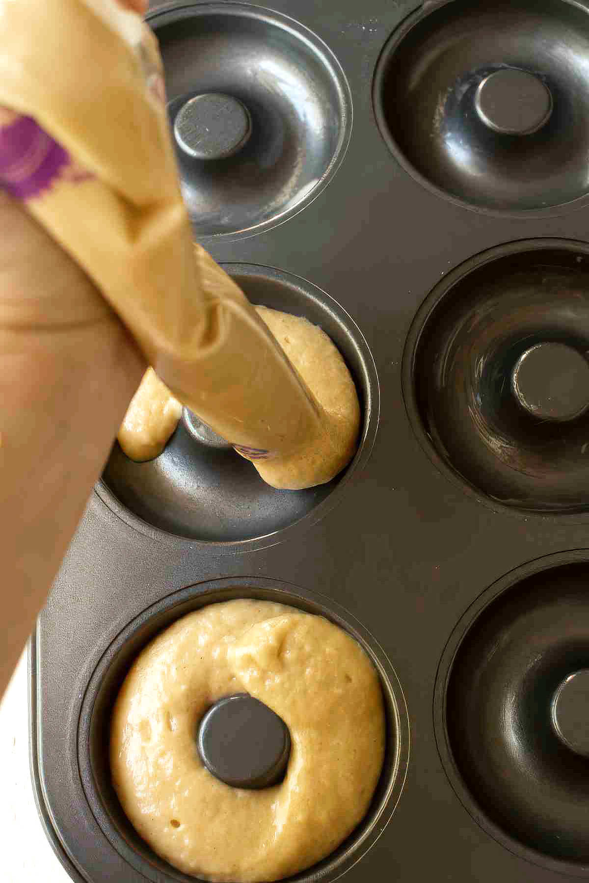 Piping apple cider donut batter into a greased donut pan before baking.