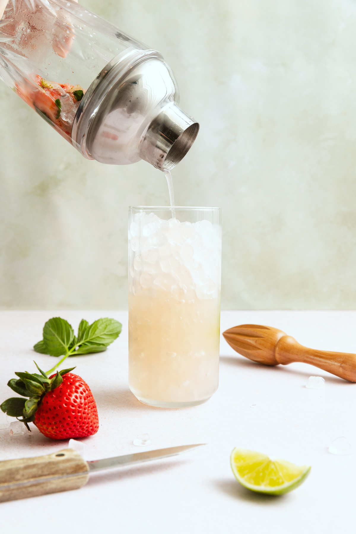 Straining a strawberry mojito mixture over ice in a highball glass.