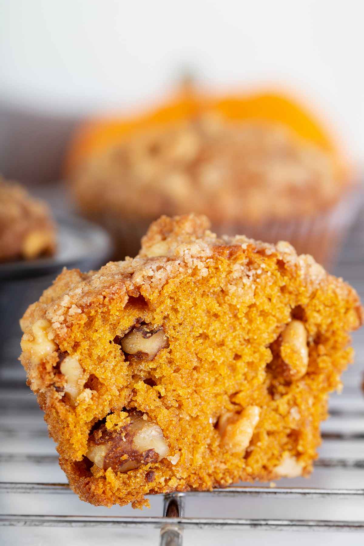 Close-up of a pumpkin muffin with pecan streusel showing the soft pumpkin crumb, chopped pecans, and cinnamon streusel topping.