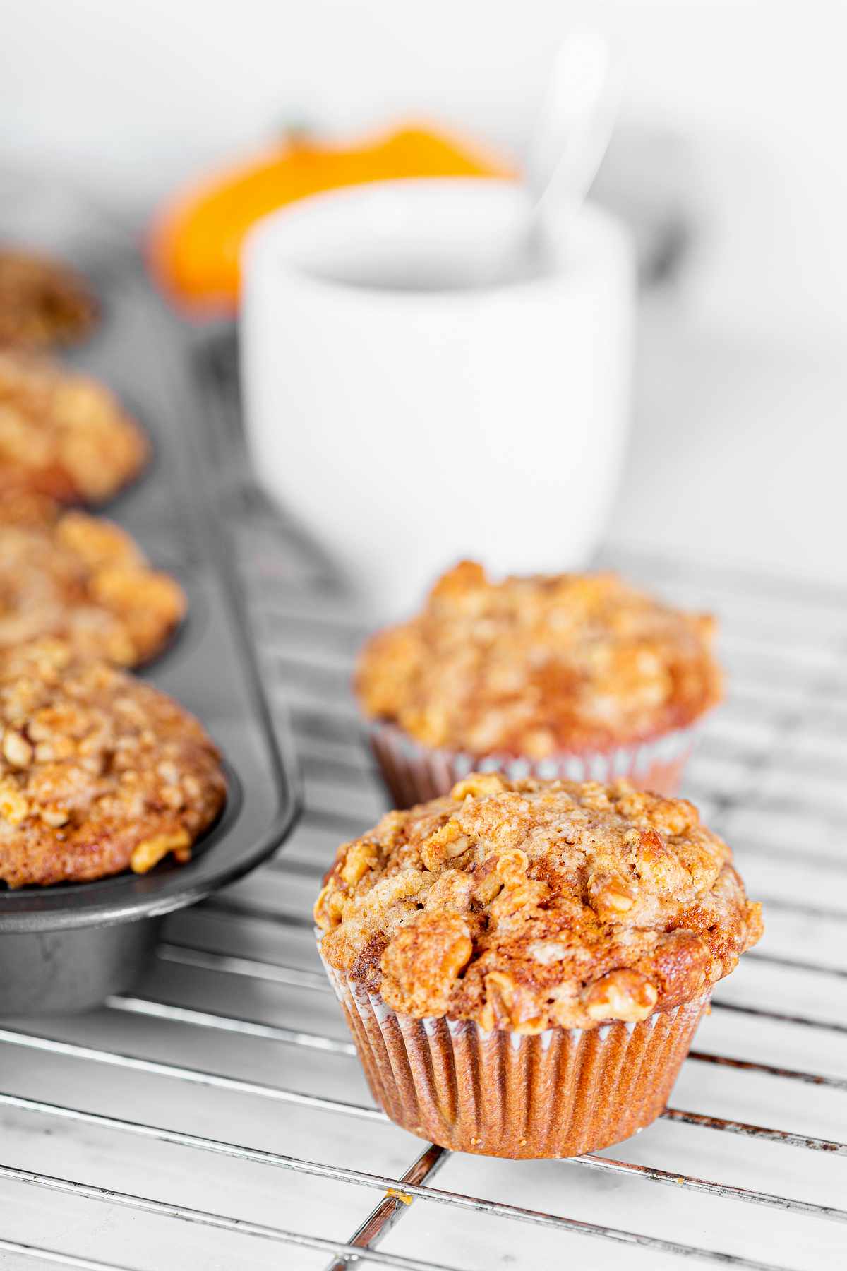 Pumpkin muffin with pecan streusel topping cooling on a wire rack beside a cup of coffee.