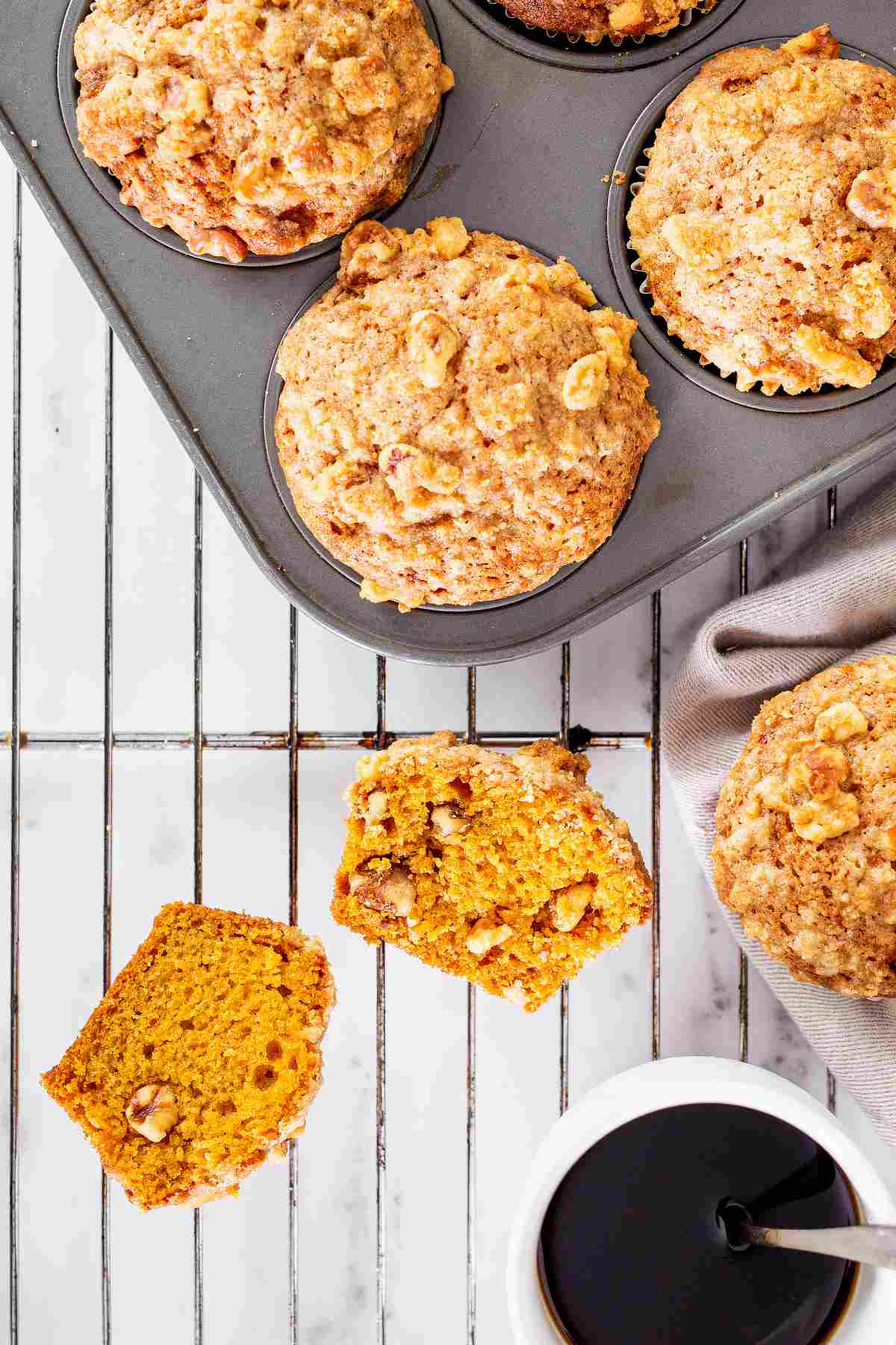 Overhead view of pumpkin muffins with pecan streusel, including a split muffin showing the moist pumpkin crumb and crunchy streusel topping.