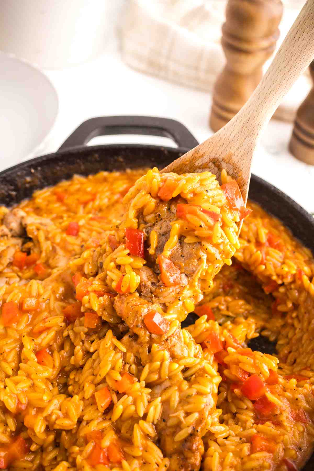 Spoon lifting creamy Cajun chicken orzo from a skillet with tender chicken and red bell peppers.