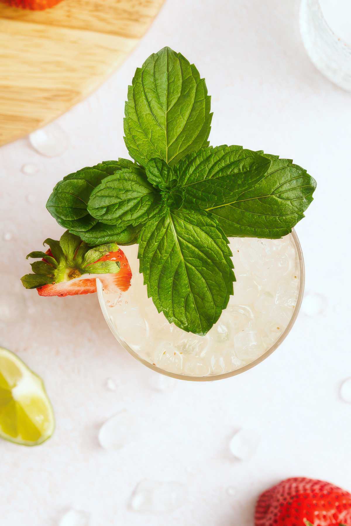 Overhead view of a strawberry mojito garnished with fresh mint leaves and a sliced strawberry over crushed ice.