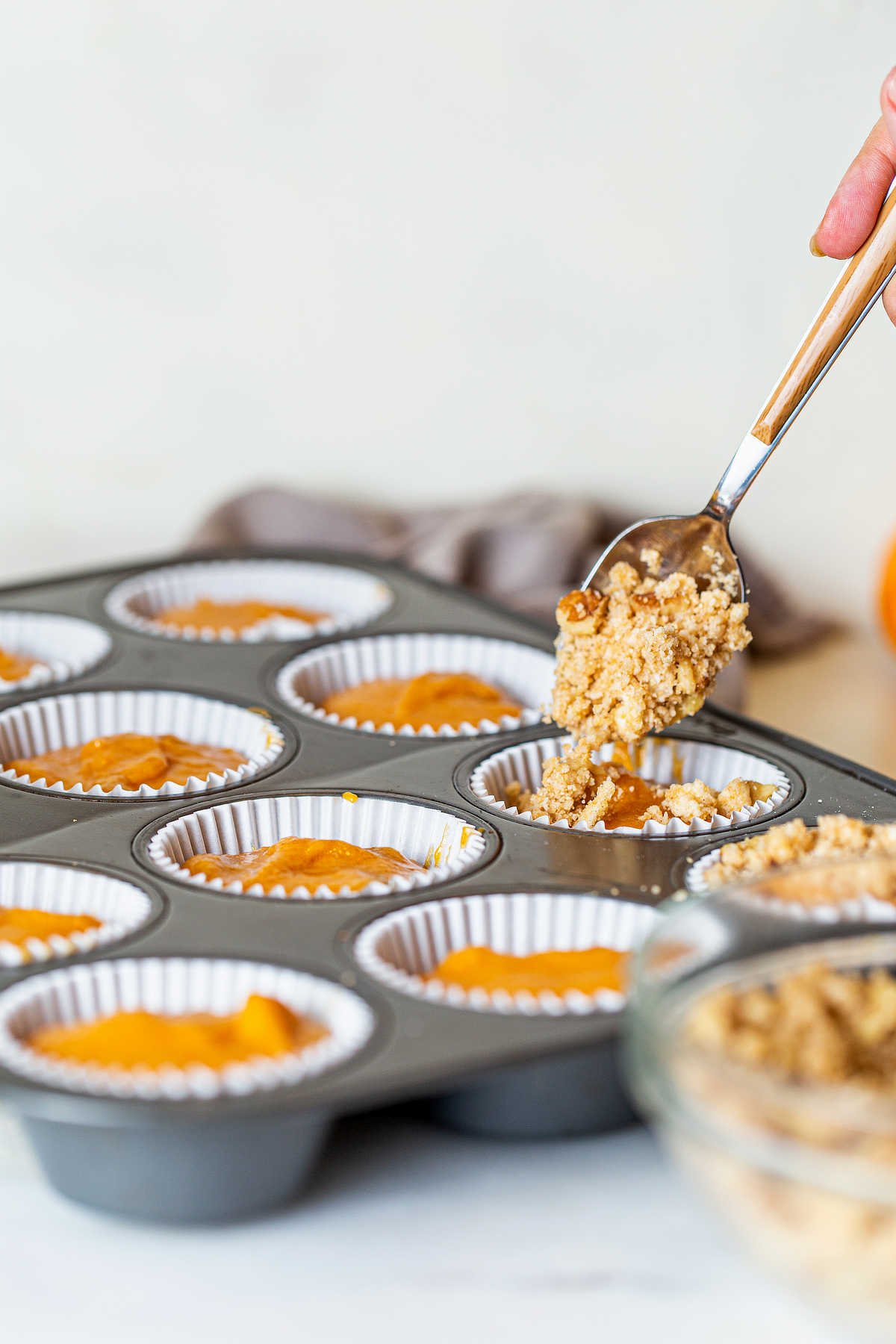 Sprinkling pecan streusel over pumpkin muffin batter before baking.