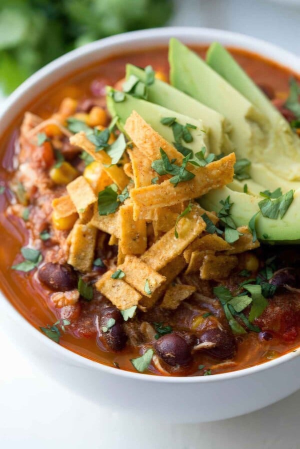 Bowl of chicken enchilada soup topped with avocado, crispy tortilla strips, and chopped cilantro.