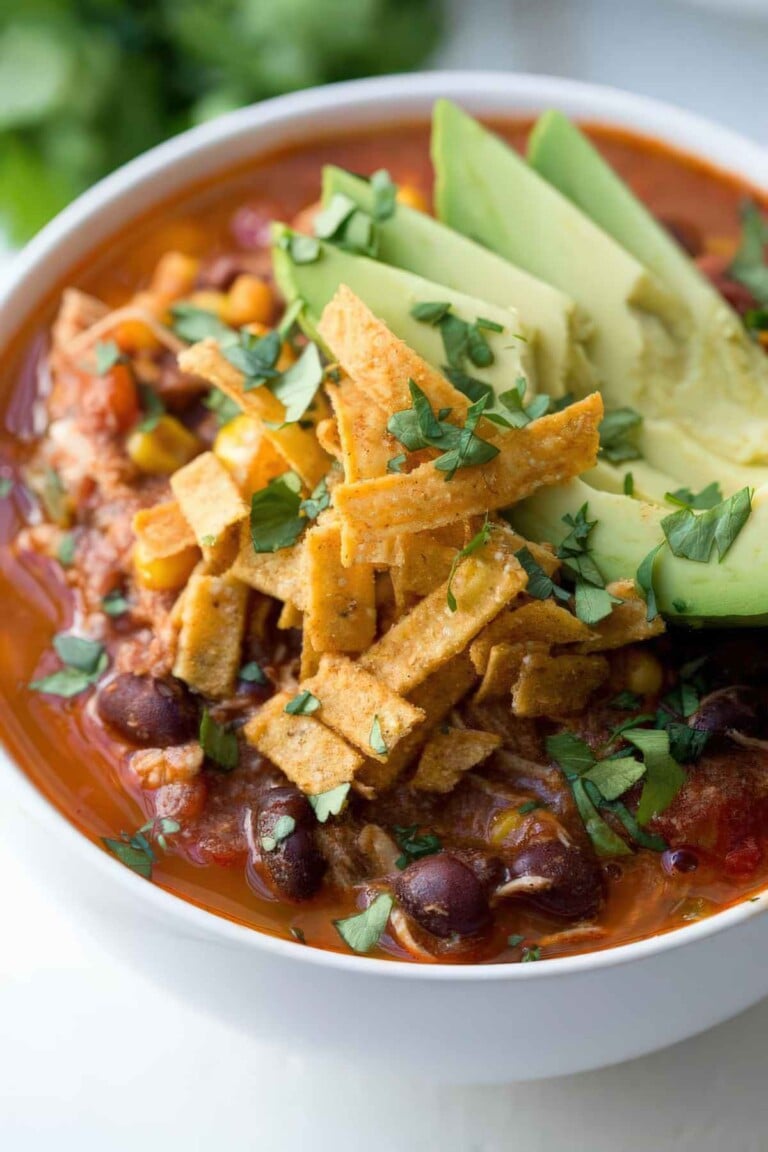 Bowl of chicken enchilada soup topped with avocado, crispy tortilla strips, and chopped cilantro.