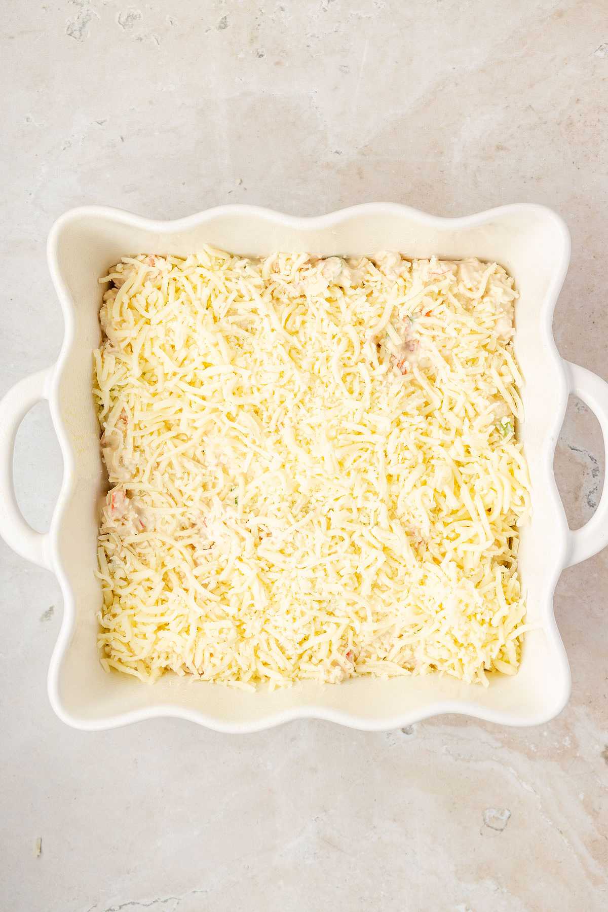Overhead view of crab rangoon dip ingredients in a glass bowl, including chopped imitation crab, cream cheese, mozzarella, sour cream, mayonnaise, garlic, and green onions.