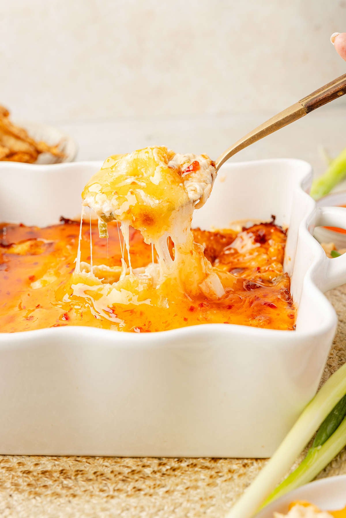 A spoon lifting a cheesy, stretchy bite of baked crab rangoon dip from the baking dish.