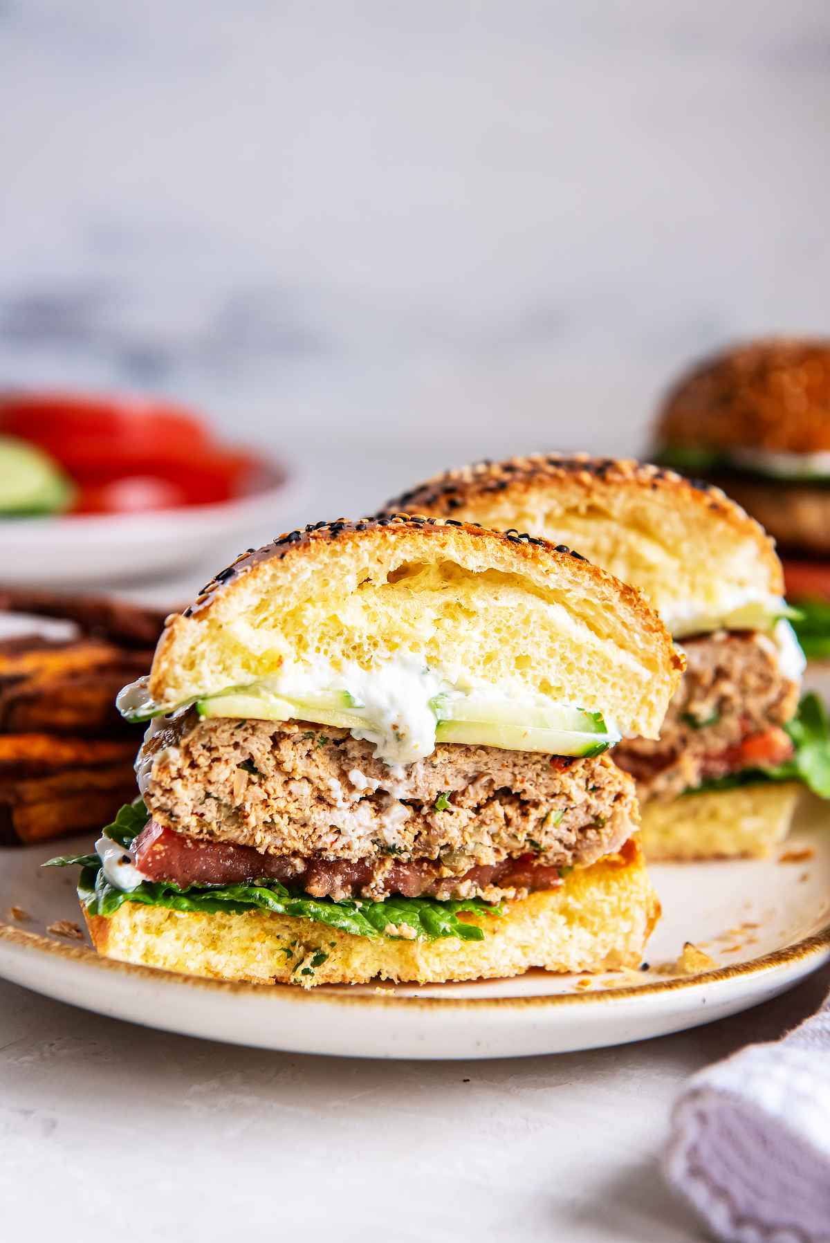 Greek turkey burger cut in half to show the cooked patty, topped with cucumber, tzatziki, tomato, and lettuce on a toasted bun.